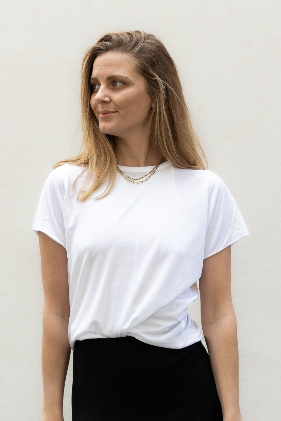 A woman wearing a white T-shirt and a long black skirt. The T-shirt is loose-fitting and made of light fabric.