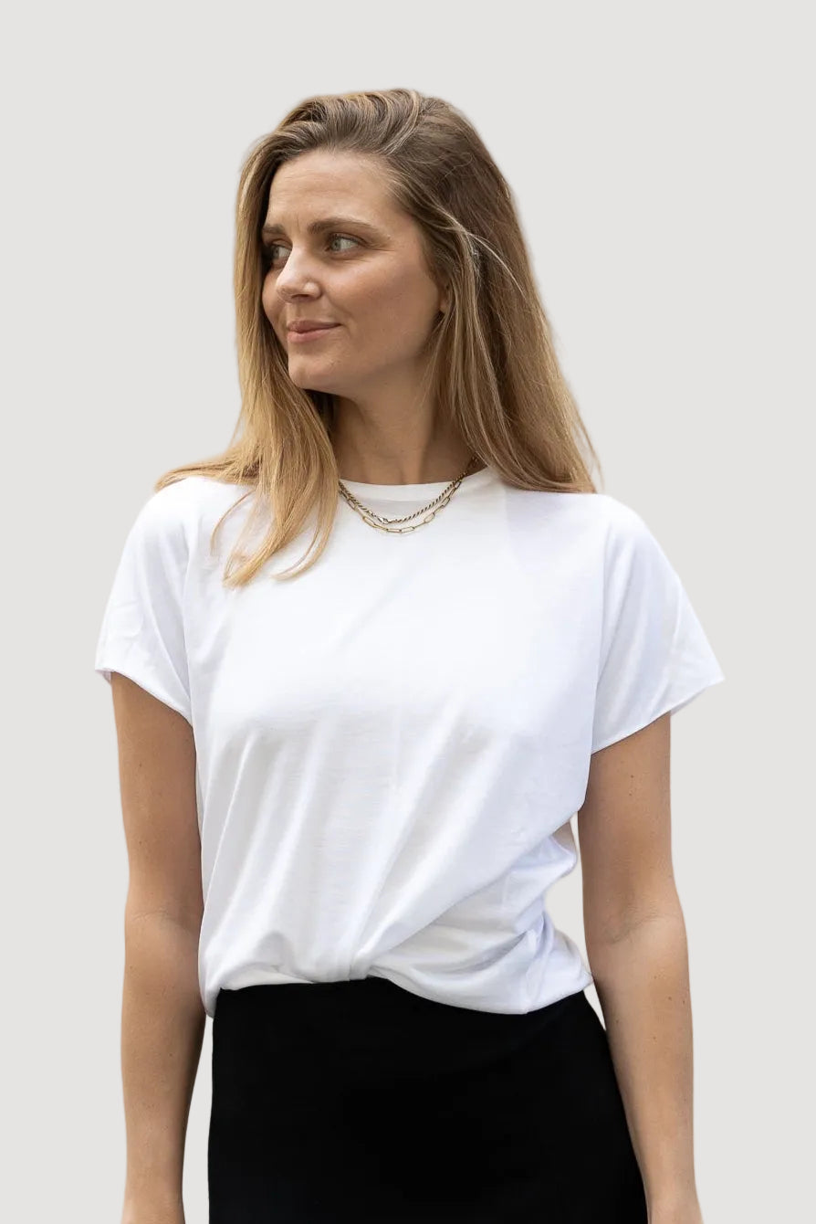 A woman wearing a white T-shirt and a long black skirt. The T-shirt is loose-fitting and made of light fabric.