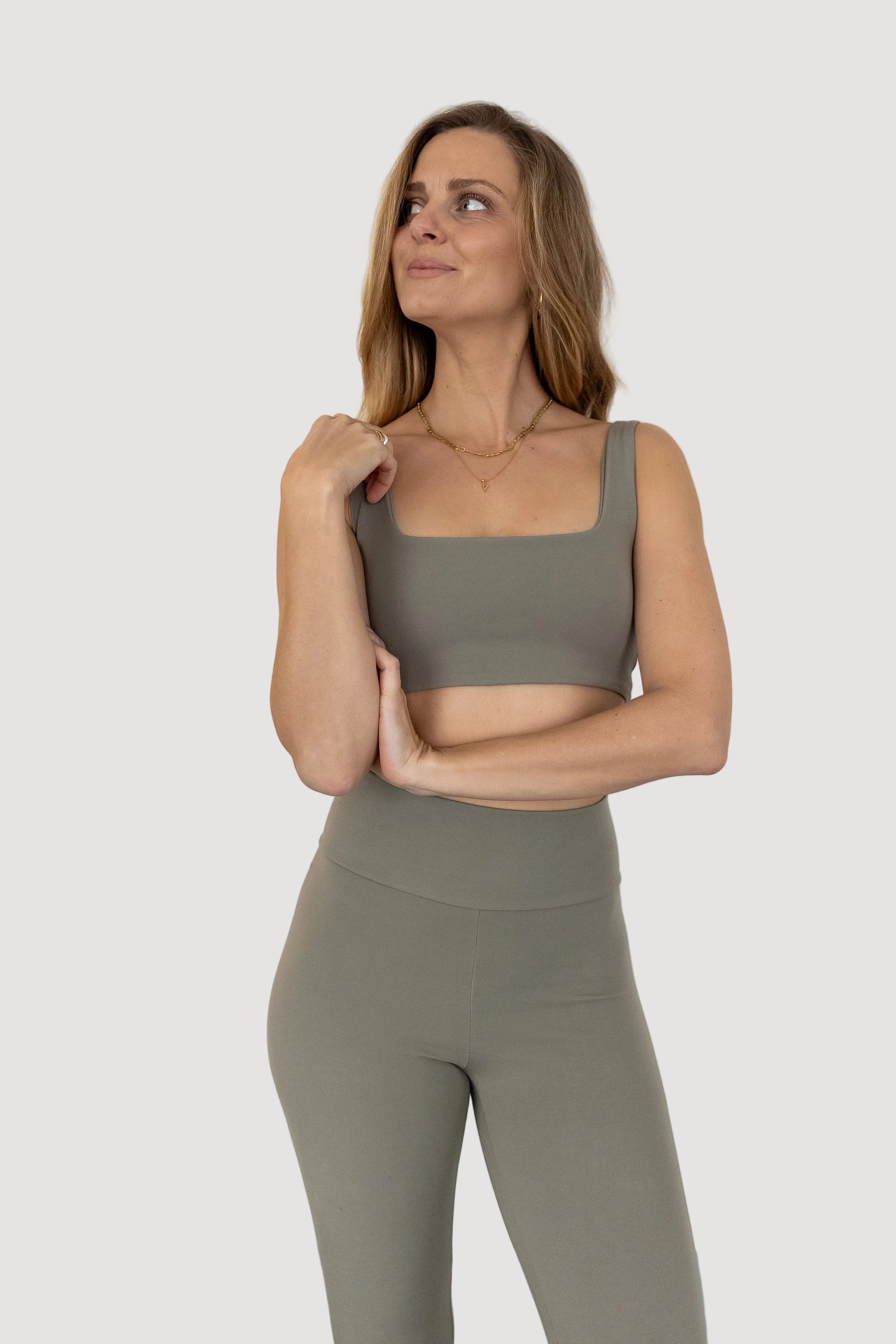 A woman wearing a green sleeveless top and matching leggings made from Tencel fabric, standing with one hand raised to her face.