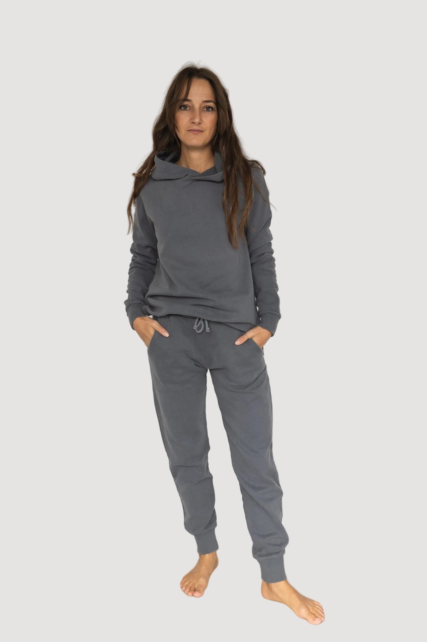 A person wearing a gray hoodie and matching pants, standing with hands in pockets.