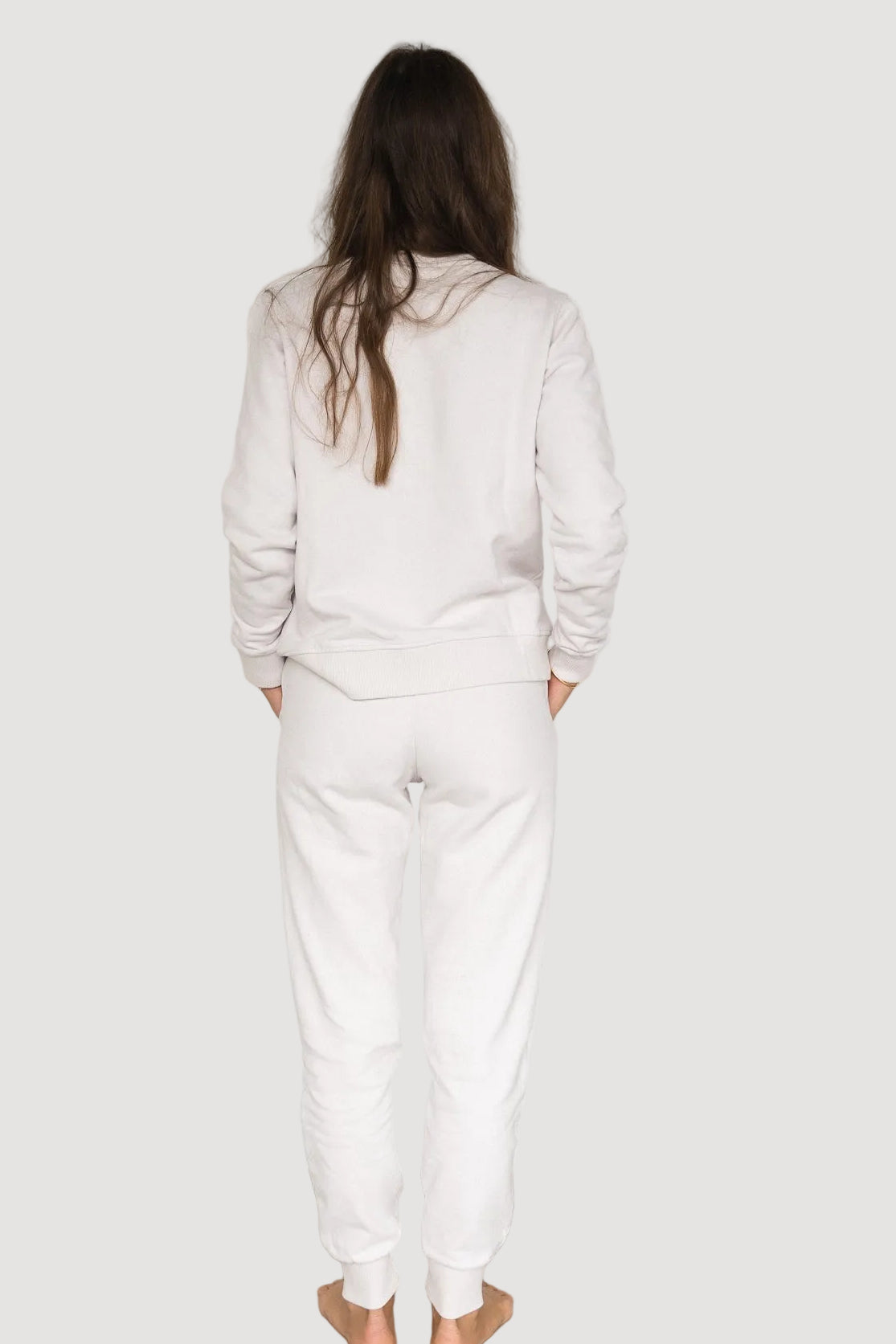 A person standing with their back to the camera, wearing white baggy pants and a matching white top, against a neutral background.