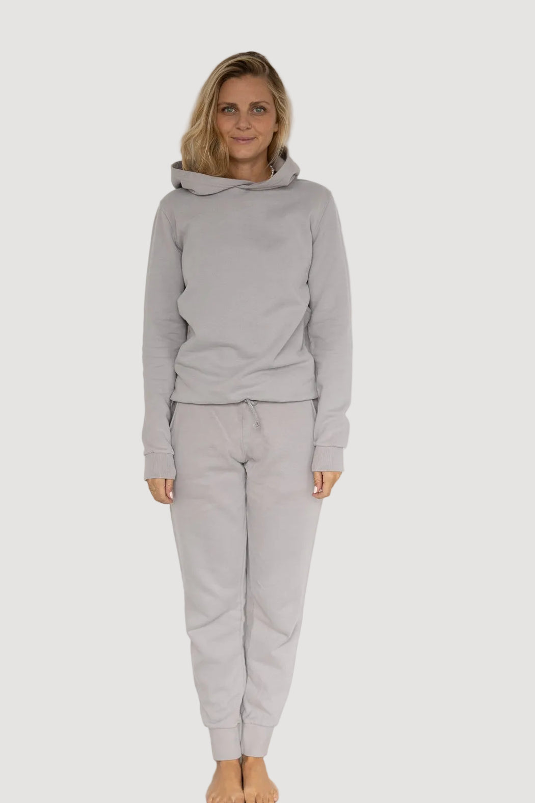 A person wearing a grey hoodie and matching pants, standing against a neutral background.