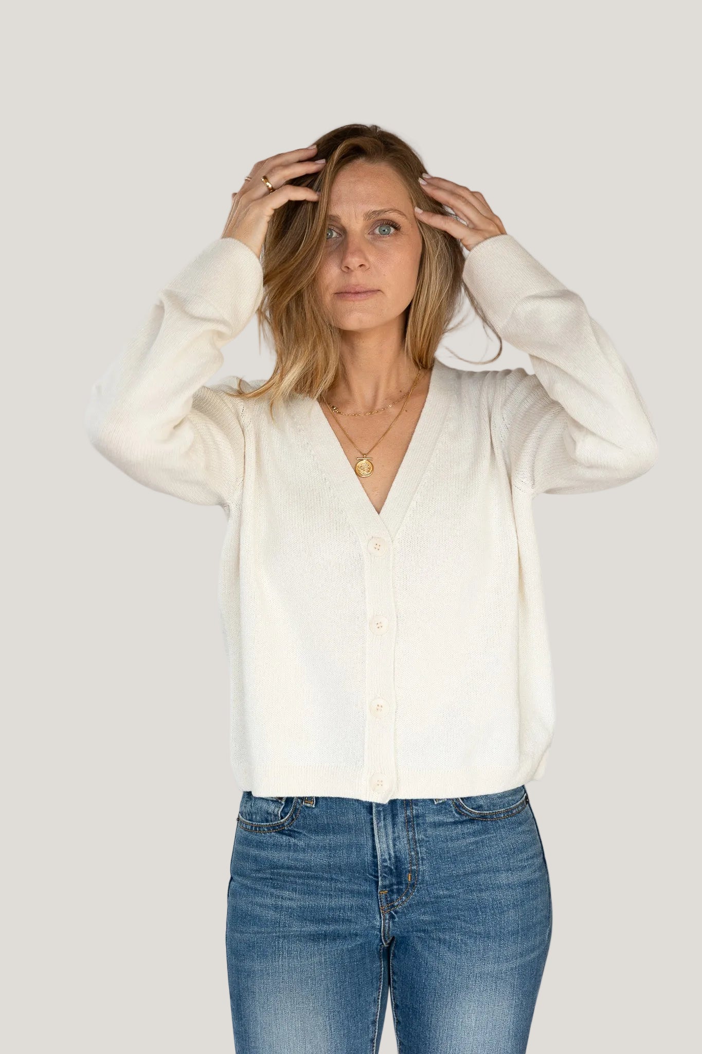 Woman wearing a white blouse and blue jeans against a plain background