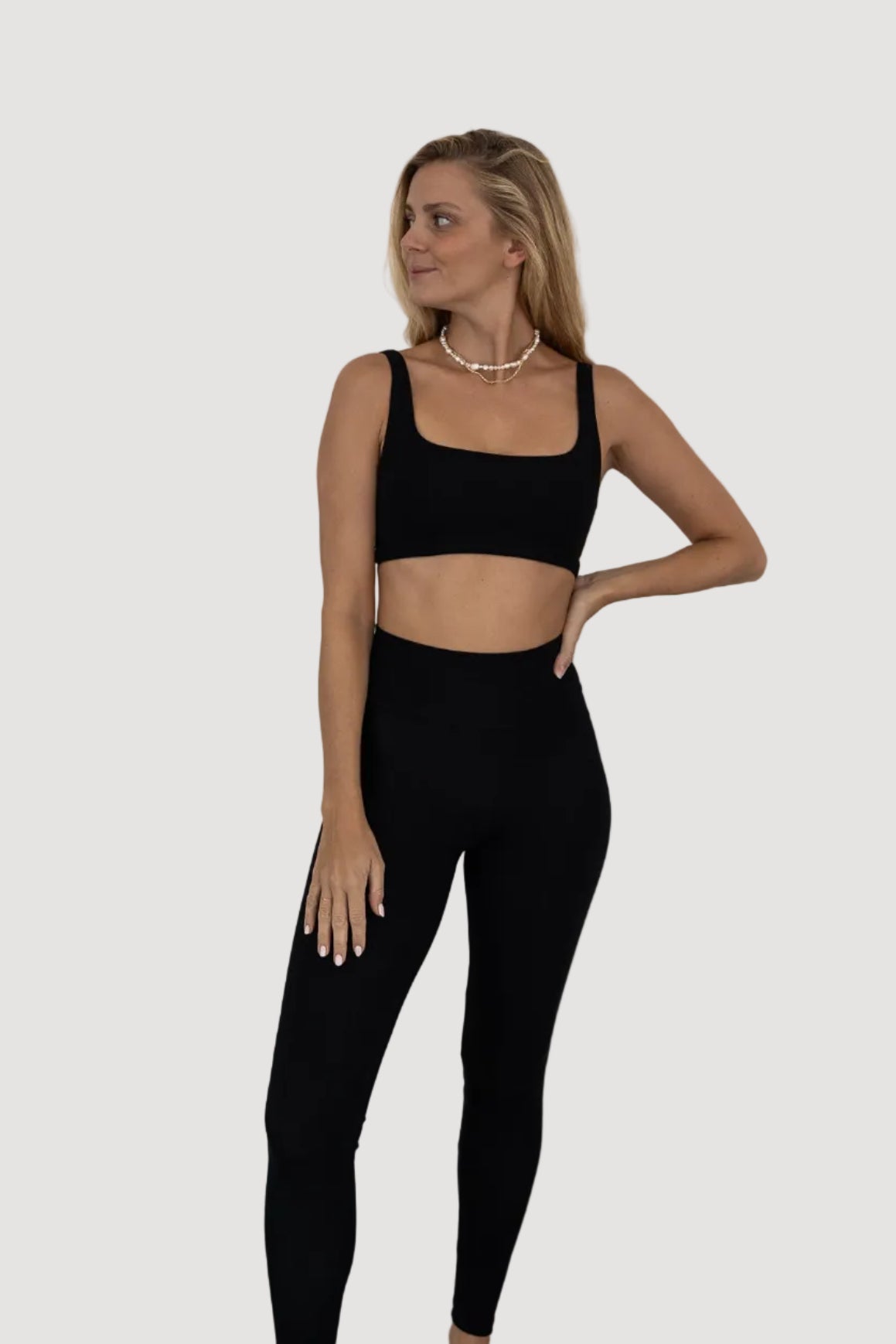 A female model wearing a black sleeveless top and matching leggings, standing against a neutral background.