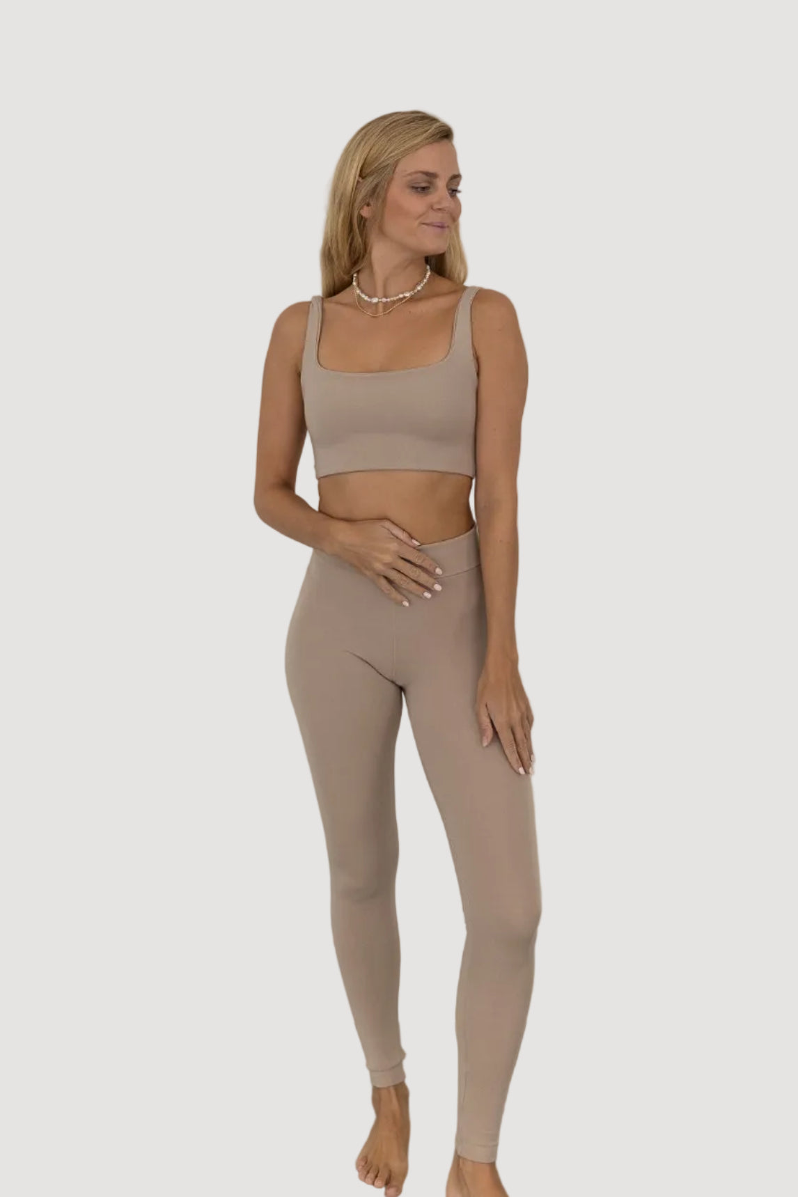 A model wearing beige high-waisted leggings and a matching crop top, standing against a plain background.