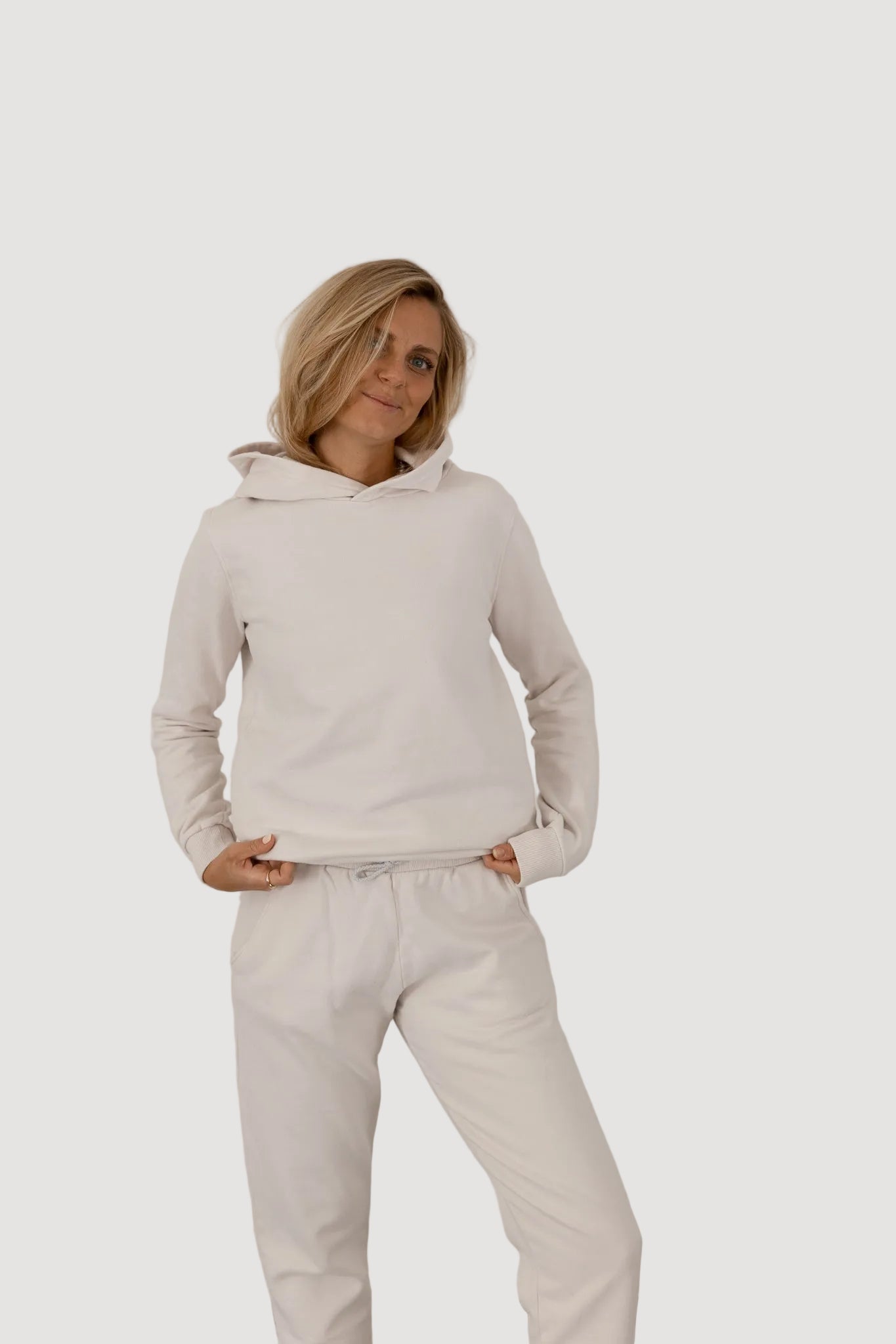 A person wearing a white oversized hoodie with the hood on, paired with white pants, standing against a neutral background.