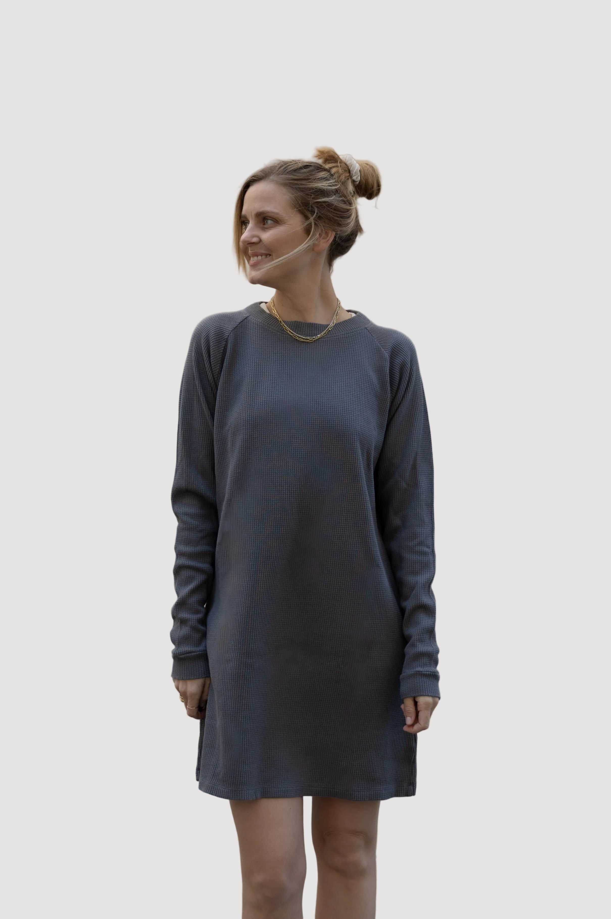 A woman wearing a dark grey dress with long sleeves, standing against a neutral background.