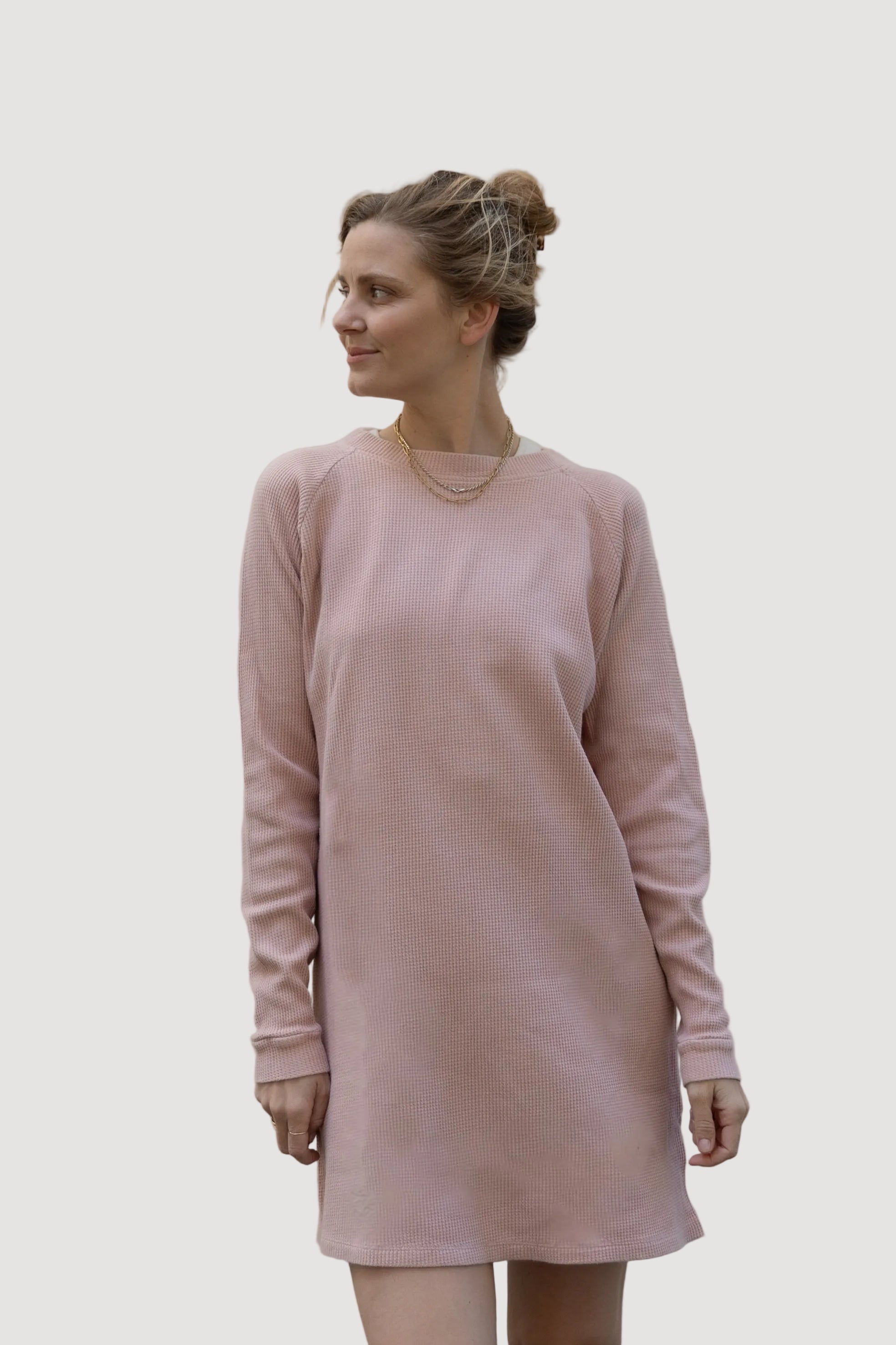 A person wearing a rose-colored, long-sleeved, knee-length dress, standing against a neutral background.