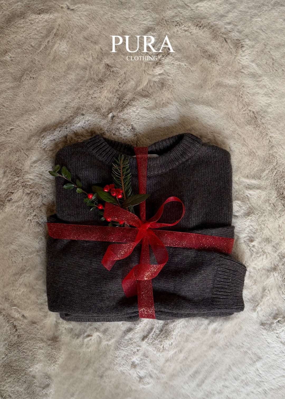 Folded dark gray garment with a red ribbon on a textured stone surface, featuring the brand 'Pura'.