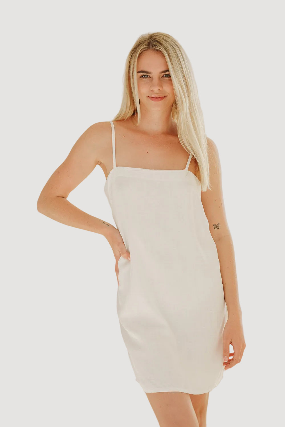 A woman wearing a white, spaghetti strap, mini dress with a straight neckline.