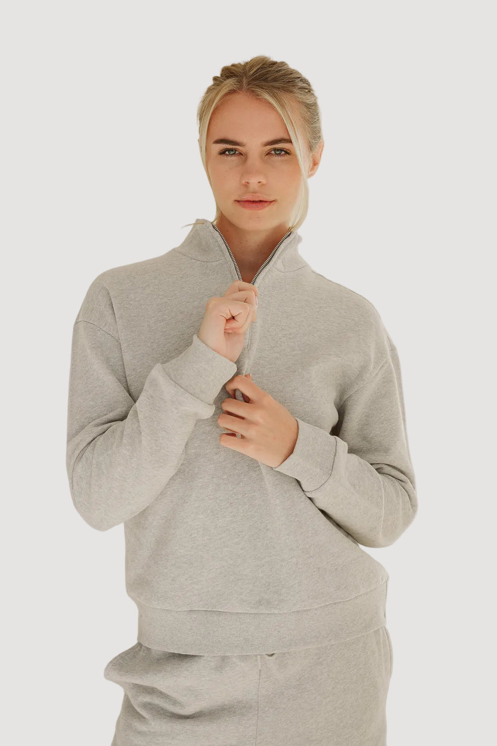 A person wearing a light grey half zip sweater, standing against a neutral background.