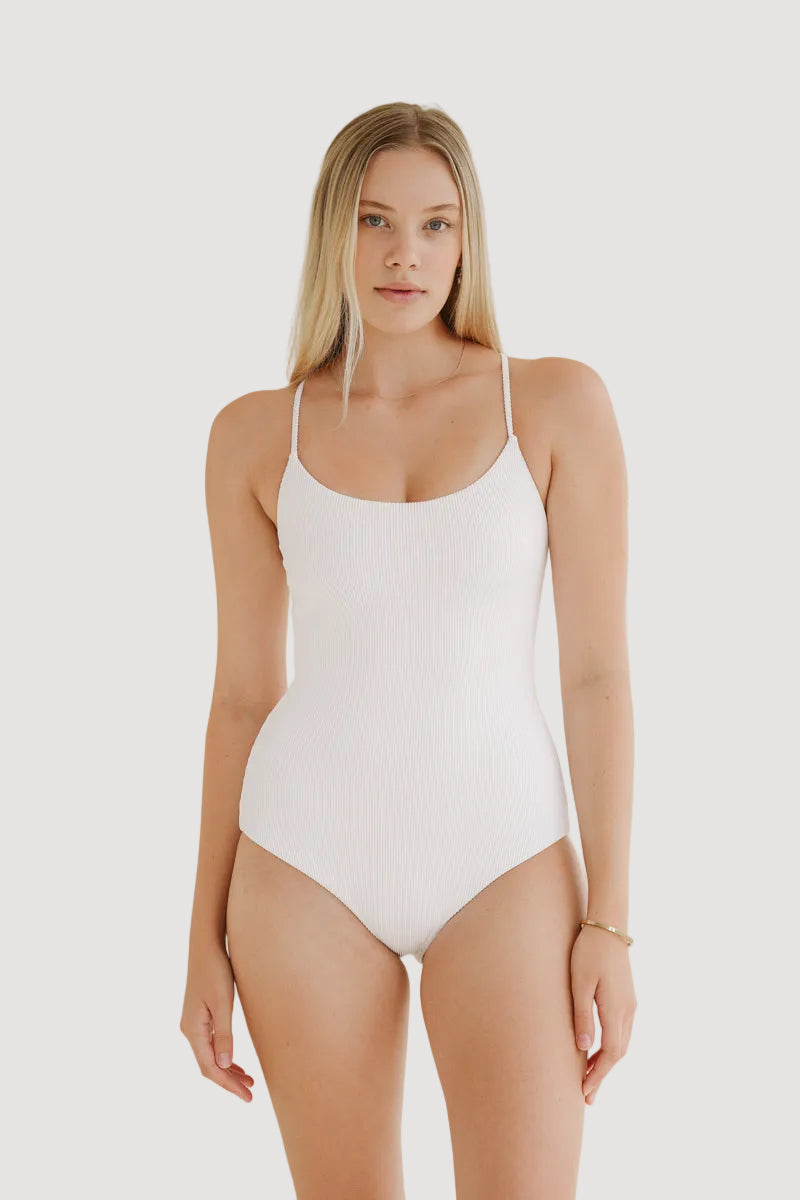 A female model wearing a white one-piece swimsuit with thin straps.