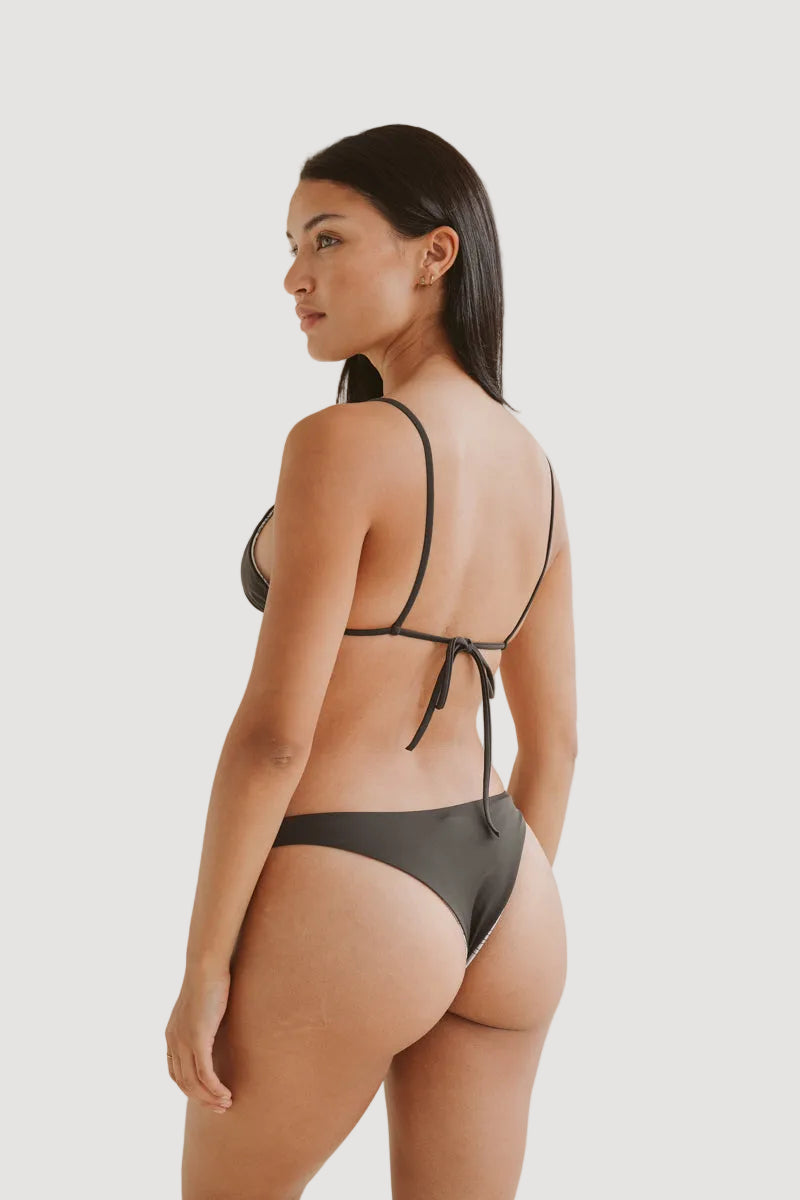 This image features a model showcasing the "DENIA BOTTOM OBLIO," a stylish and eco-friendly swimwear bottom. The swimwear is crafted from soft Italian fabric, a blend of 80% recycled polyamide and 20% elastane, highlighting both sustainability and comfort.