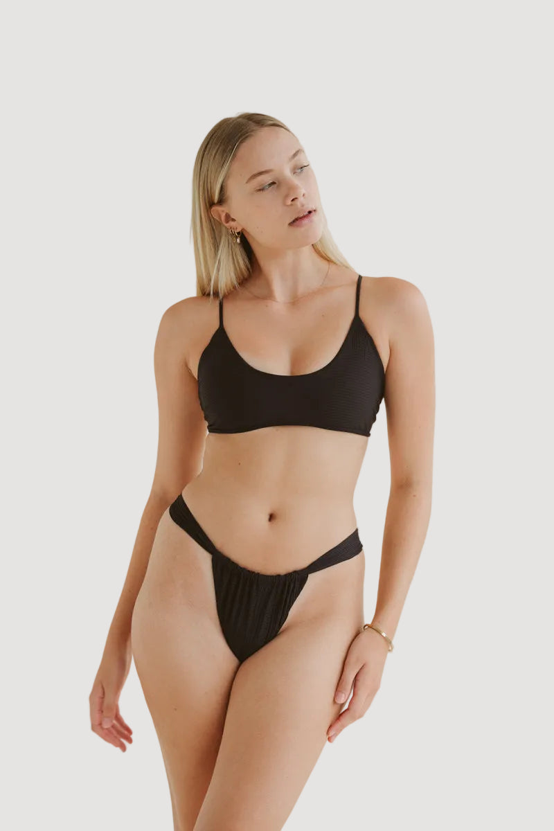 A female model wearing a black medium coverage bikini top with adjustable straps and a seamless cut.