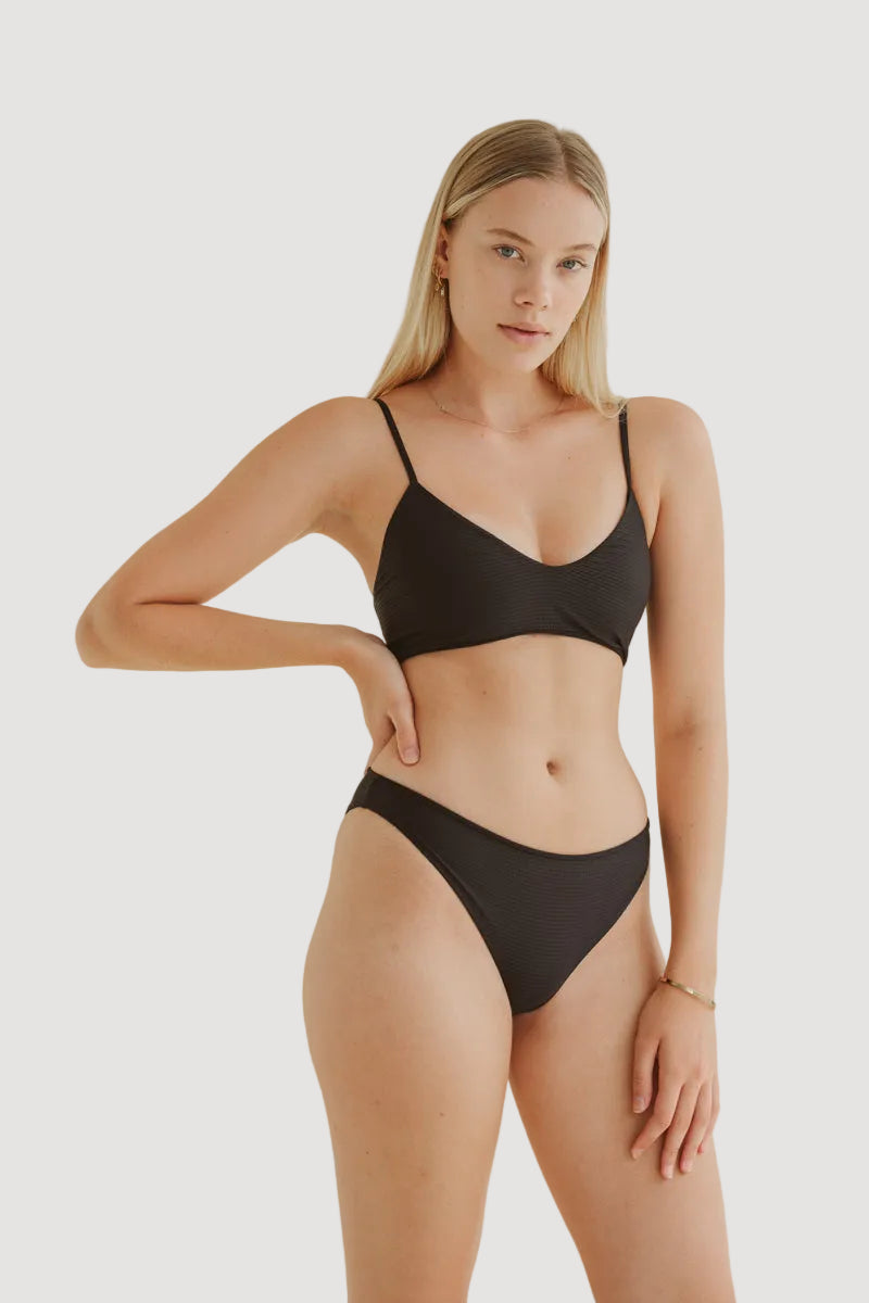A model is wearing a black bikini top with adjustable straps and medium to small coverage. The top appears to have a dotted pattern and is made from soft Italian fabric.