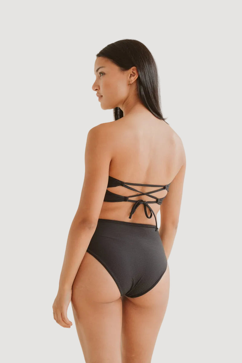 A rear view of a person wearing a black high-waisted bikini bottom with a tie at the back.