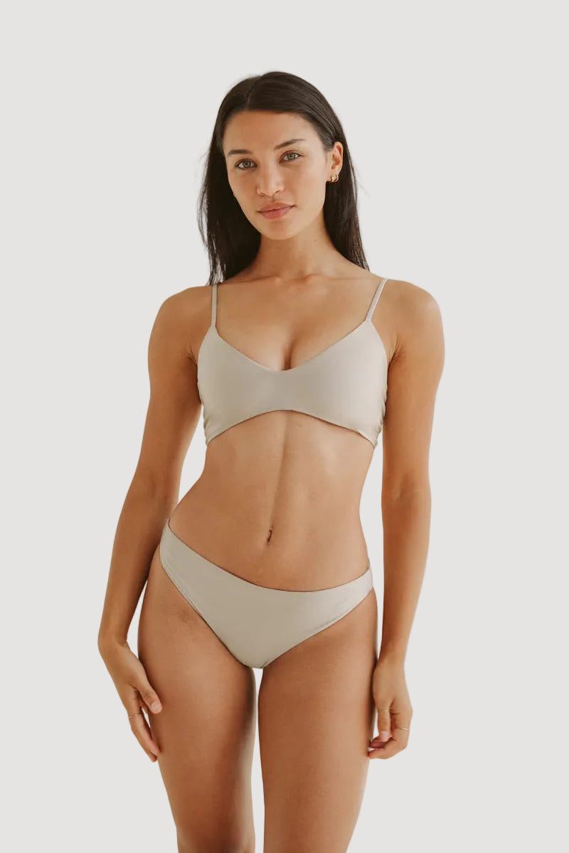 A model is wearing a beige shiny bikini top with adjustable straps, medium to small coverage, and matching bottoms.