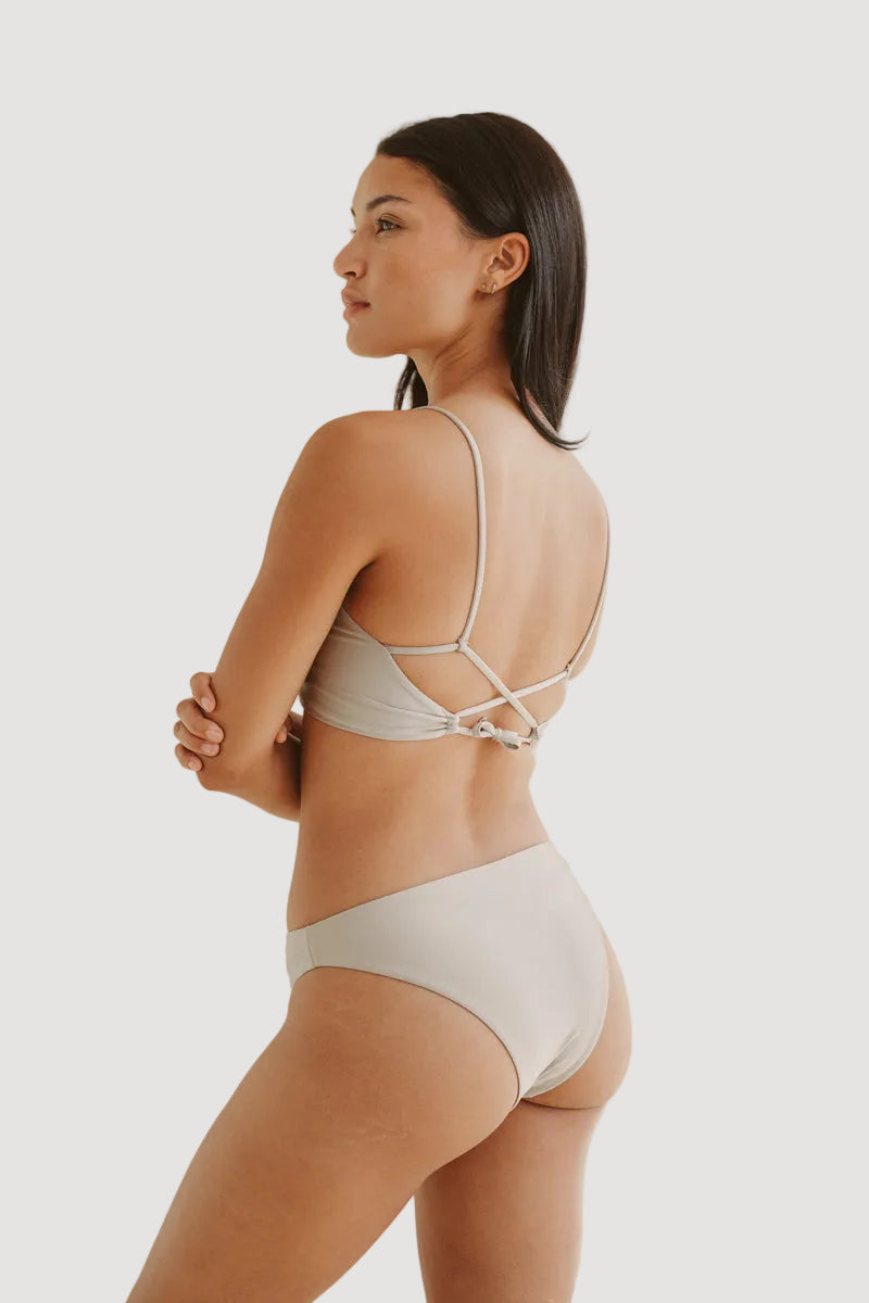 A model is wearing a beige shiny bikini bottom with a medium to small coverage. The swimwear is made from soft Italian fabric and features a seamless cut and a strappy back design.