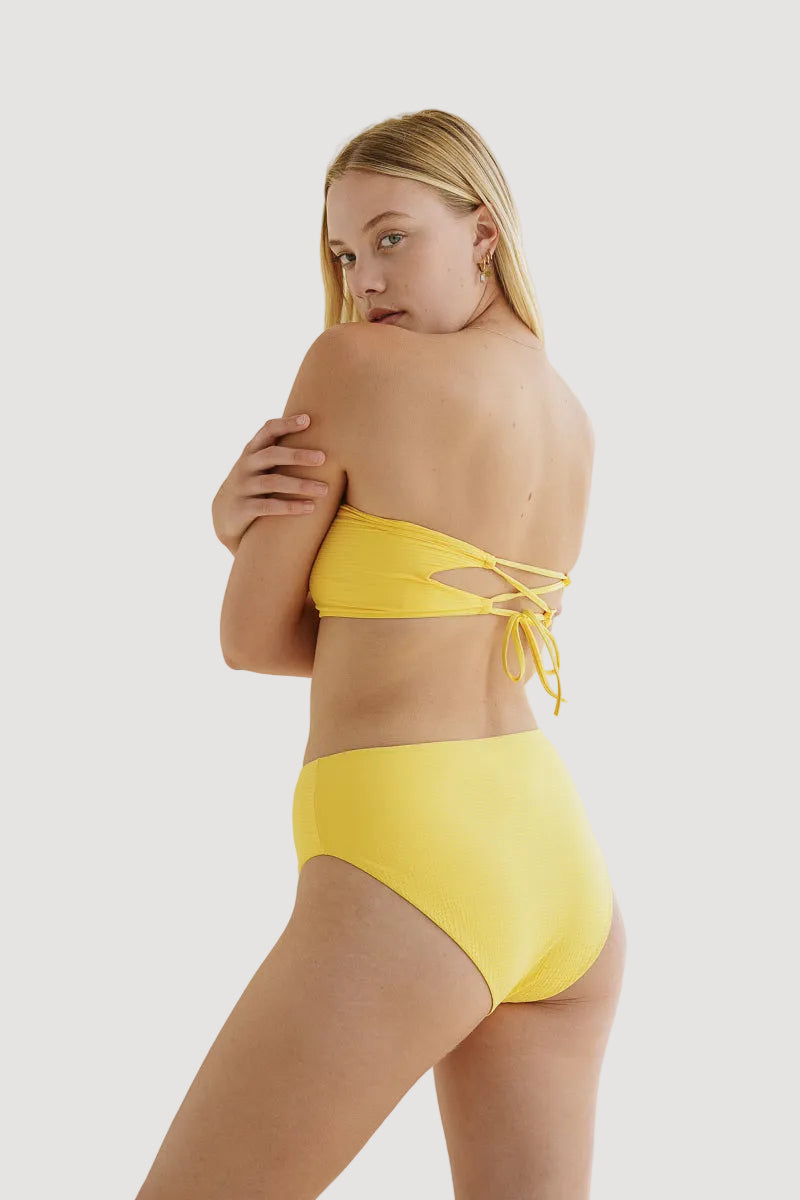 A model wearing a yellow high-waisted bikini bottom with a seamless cut and tie at the back.