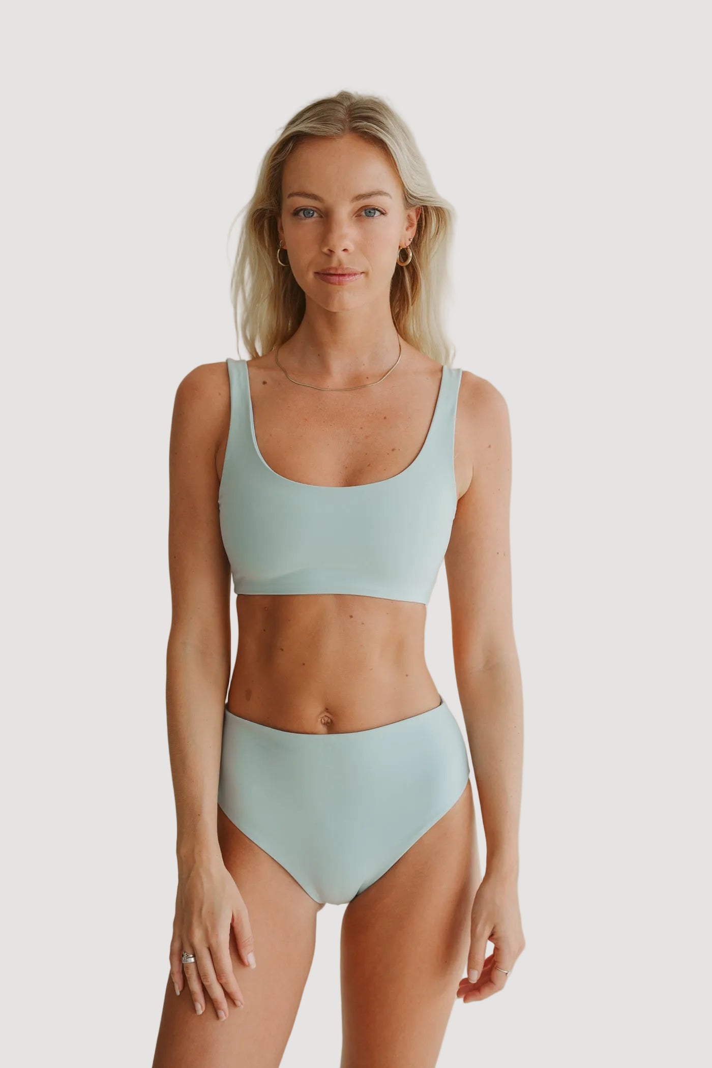 A woman wearing a light blue bikini top and matching bottoms, standing against a neutral background.