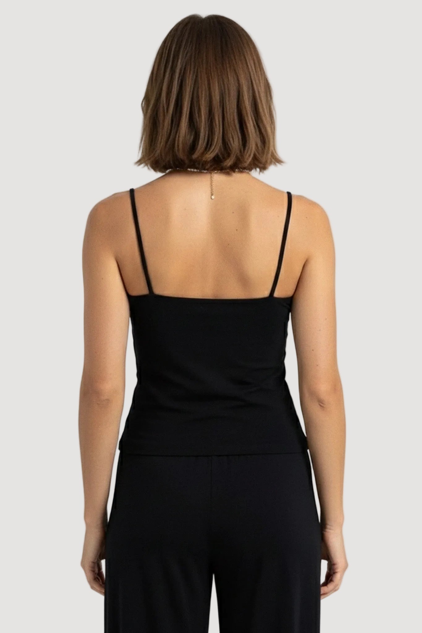 Person wearing a black sleeveless top and black pants on a white background