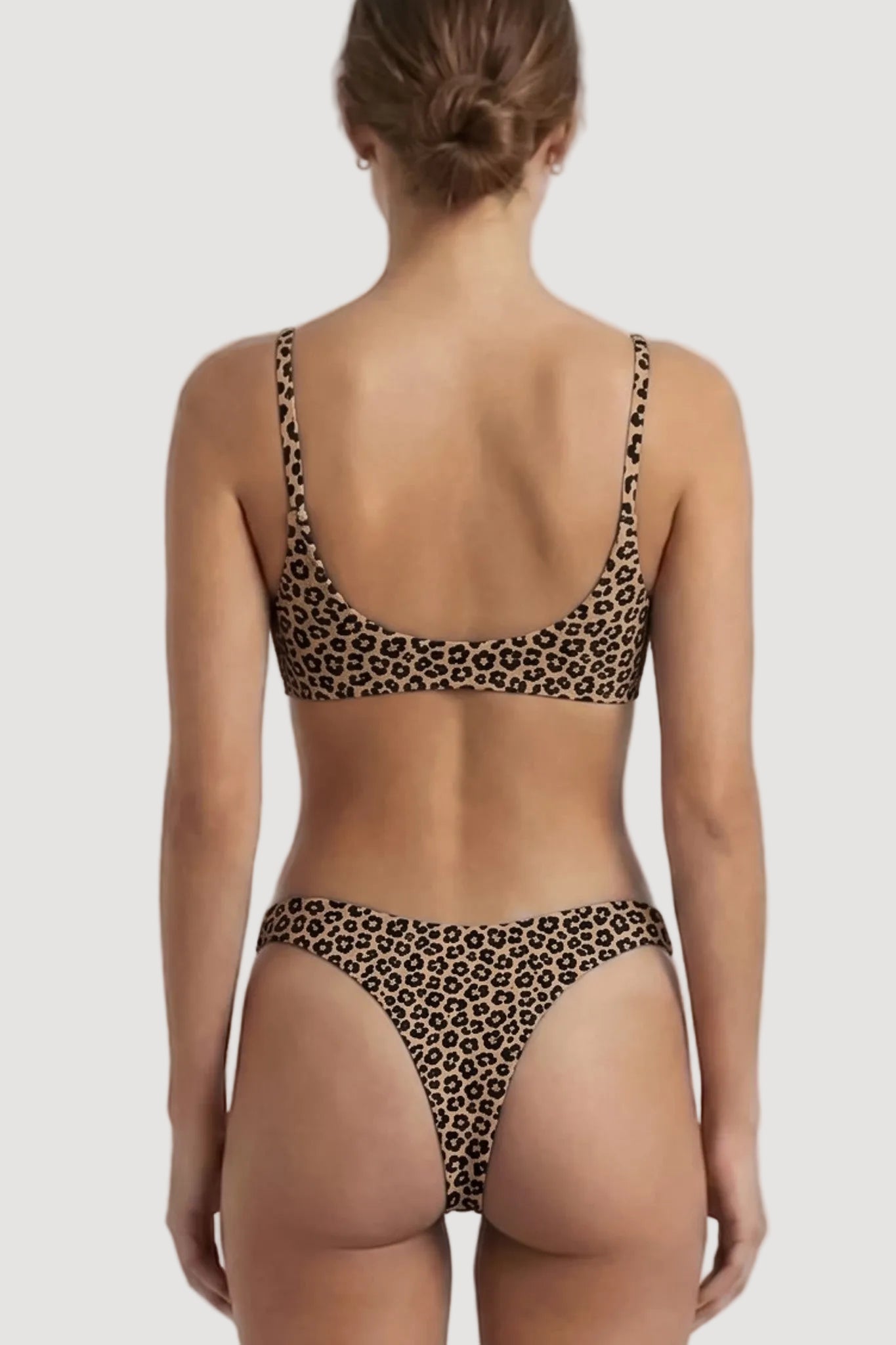 Rear view of a woman wearing a leopard-print bikini against a light gray studio background.