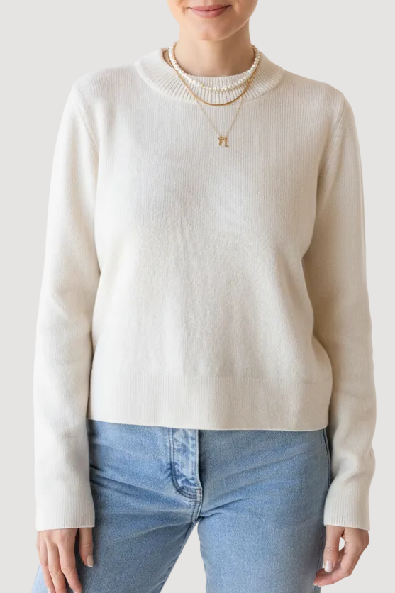Woman wearing a cream sweater and light blue jeans on a white background