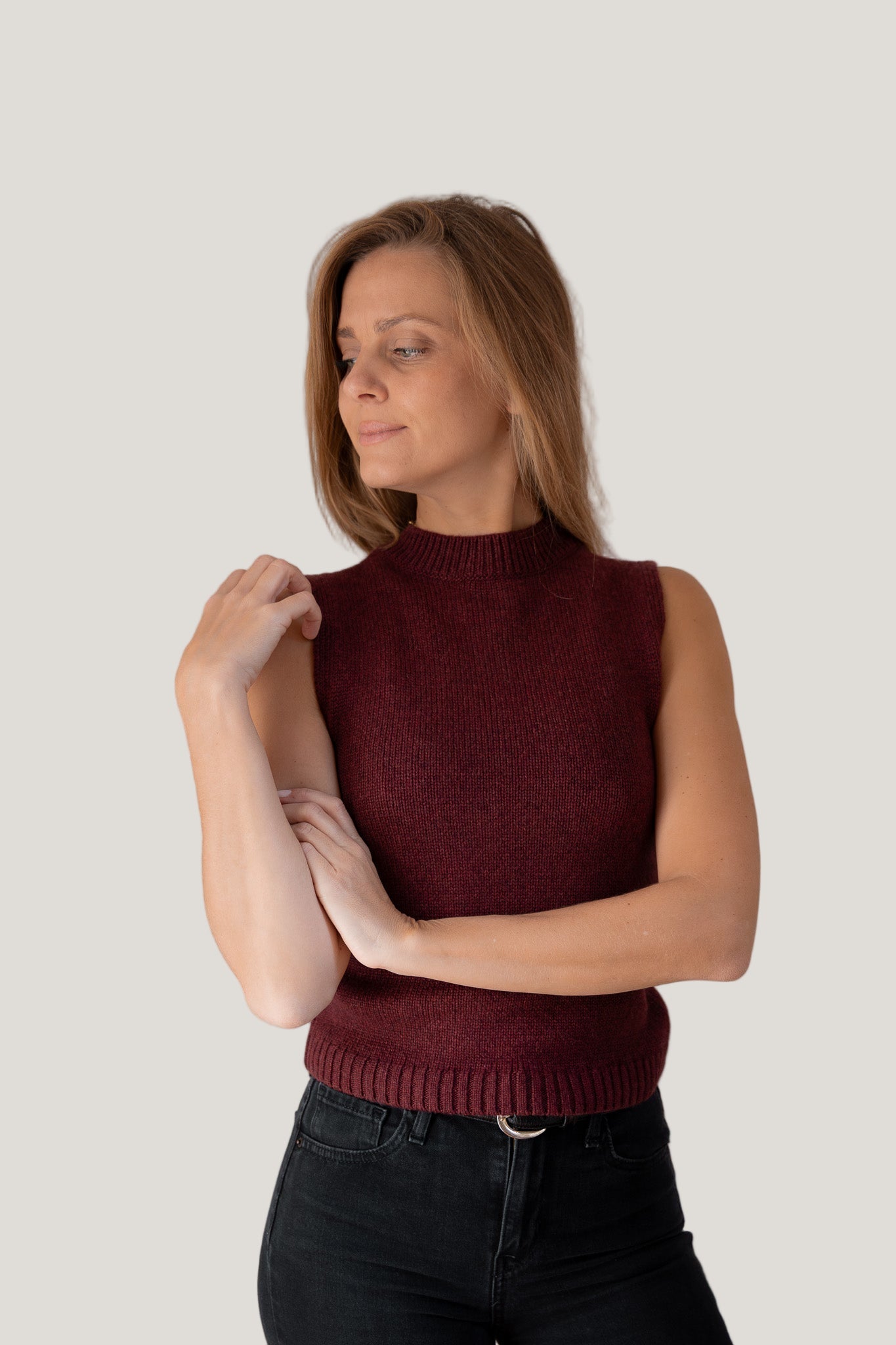 Woman wearing a burgundy cashmere sleeveless sweater against a plain background