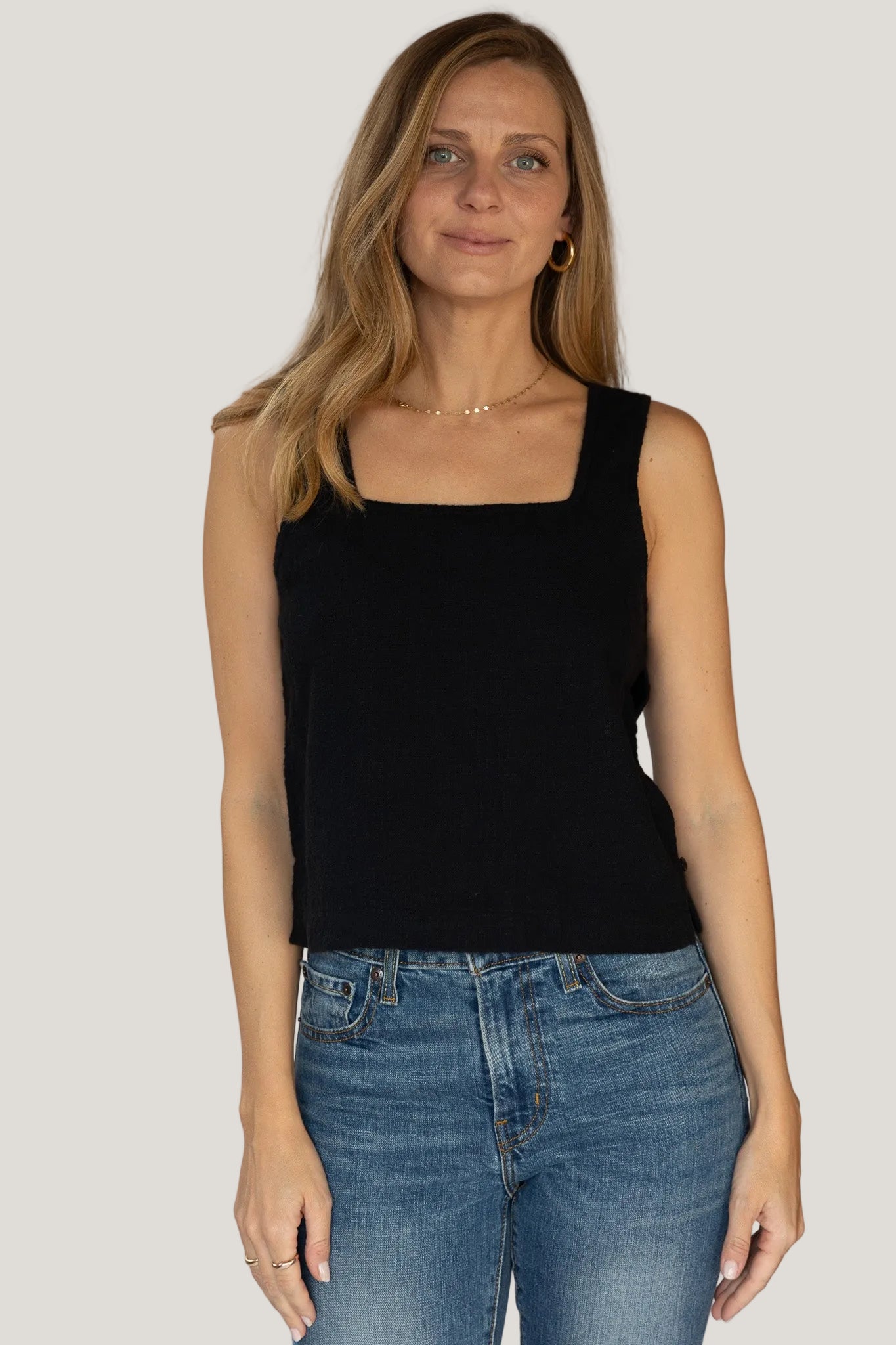 Woman wearing a black sleeveless top and blue jeans against a plain background