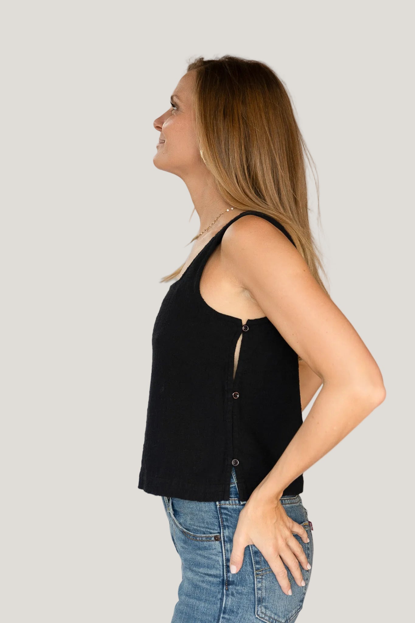 Woman wearing a black sleeveless top and blue jeans against a white background