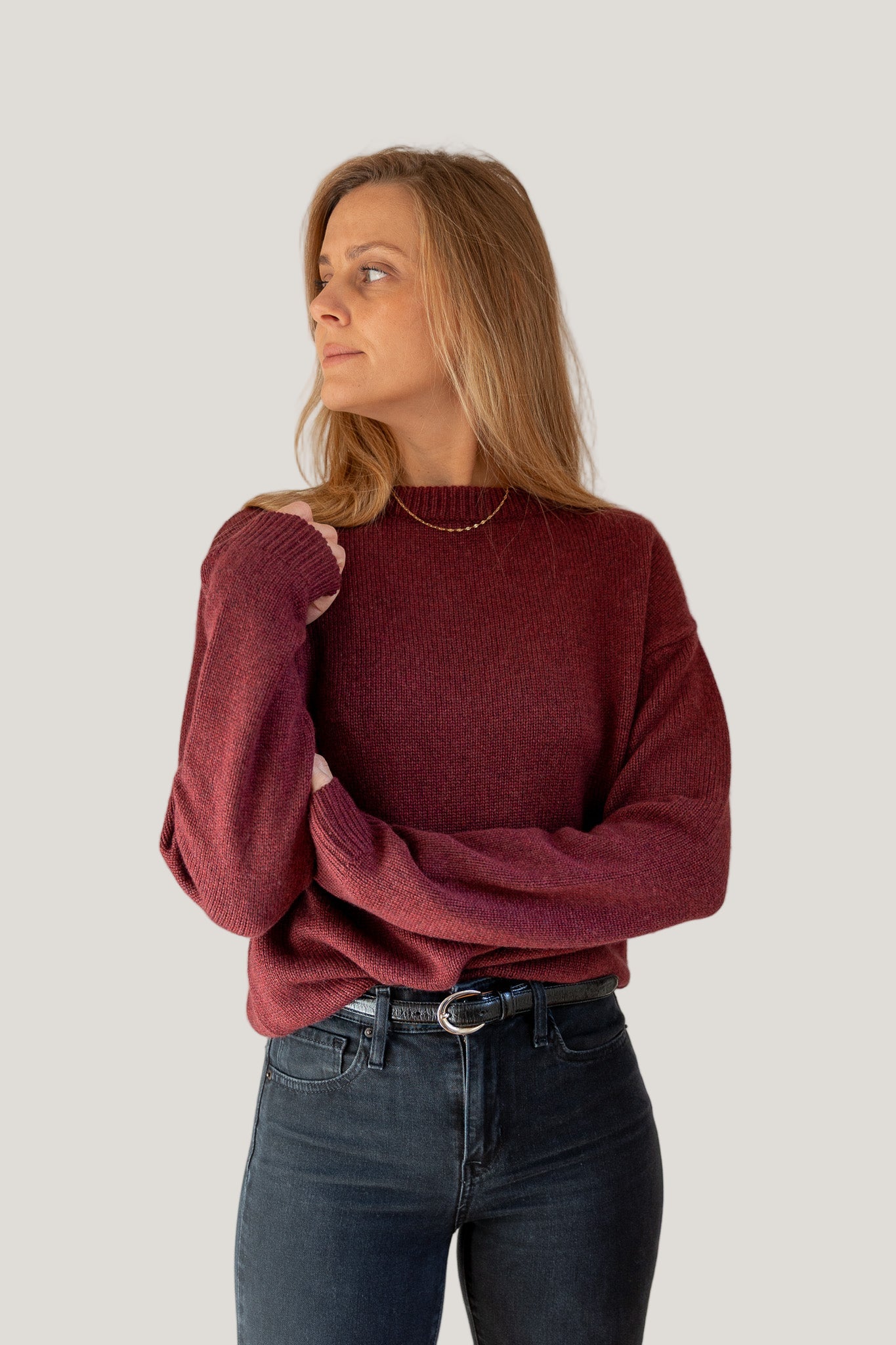 Woman wearing a burgundy sweater and dark jeans against a plain background
