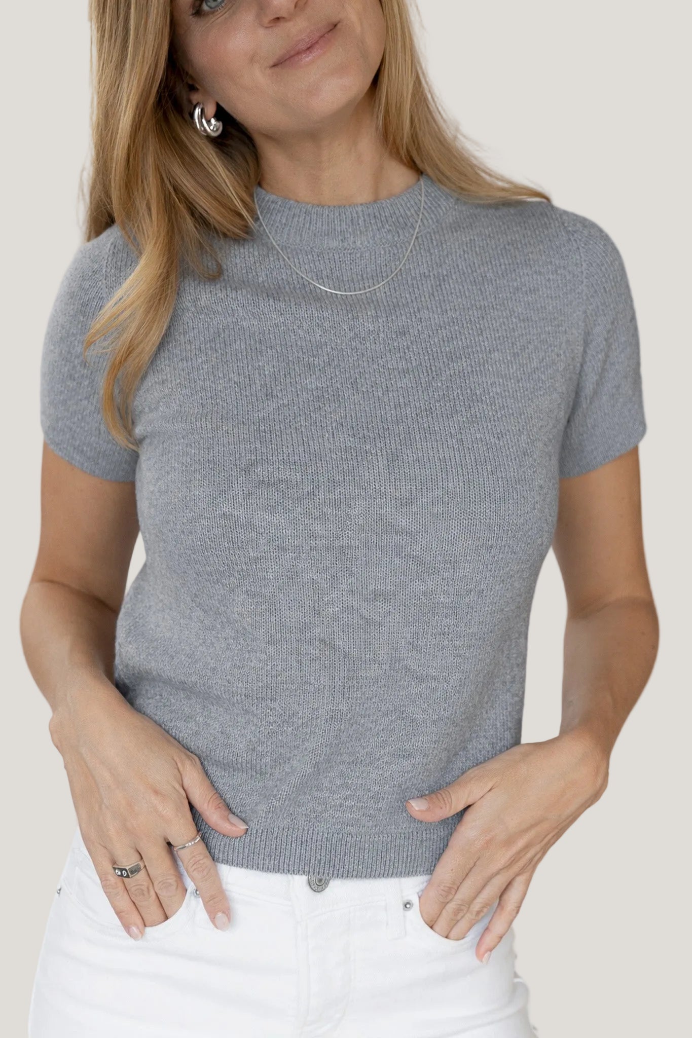 Woman wearing a gray short-sleeve knit top against a white background