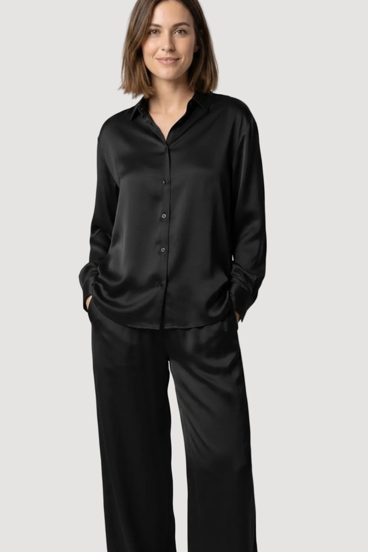 Woman wearing a black satin pajama set against a white background