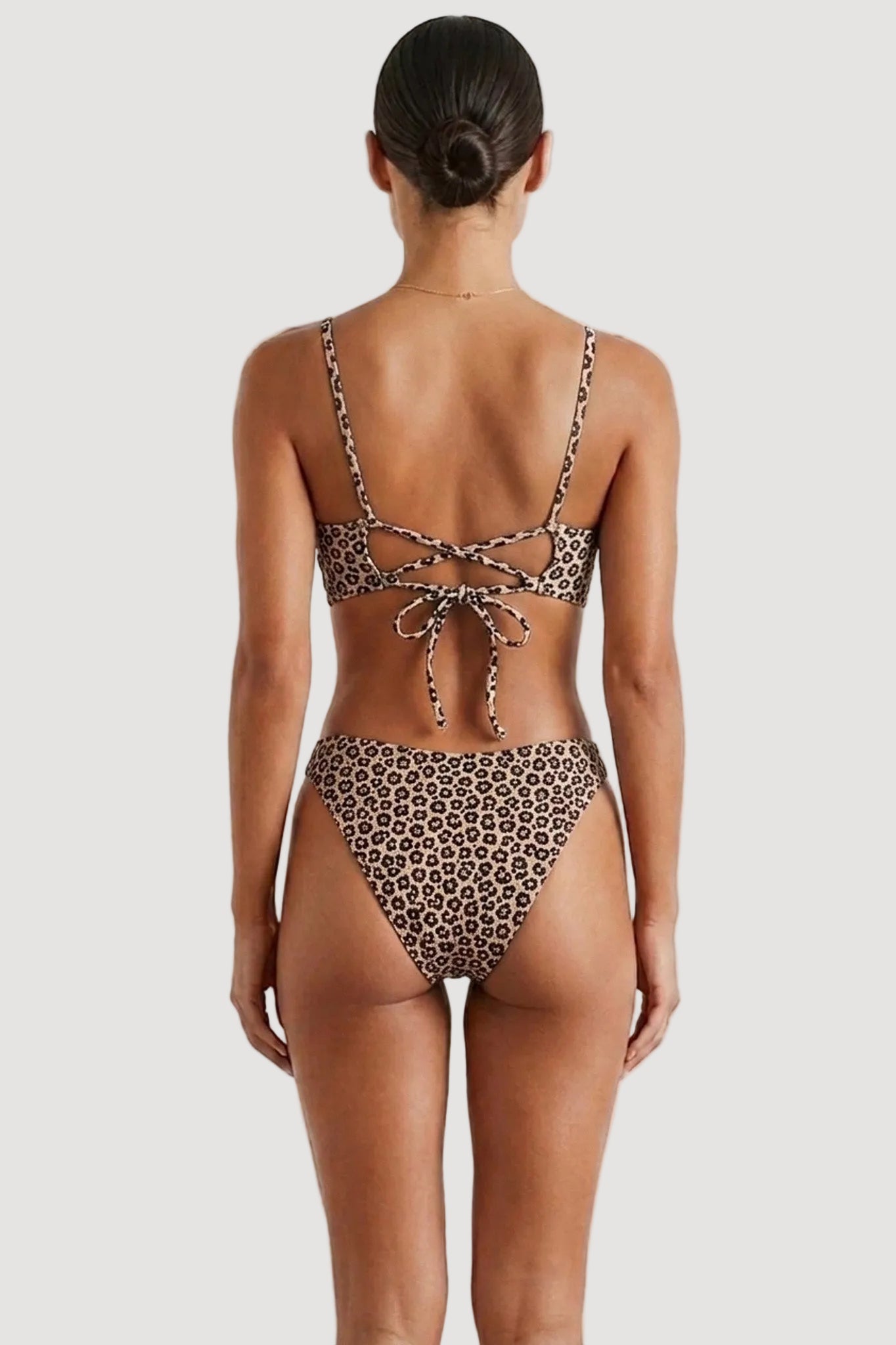 Rear view of a woman modeling a two-piece bikini with a brown, black, and beige leopard print pattern against a plain white background.