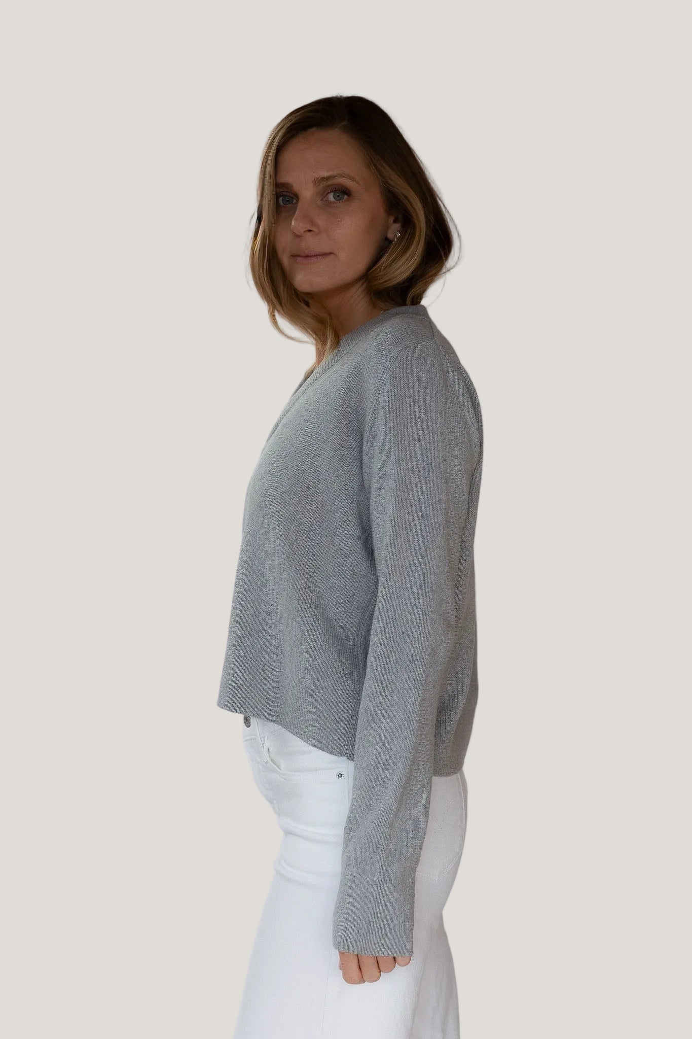 Woman wearing a gray sweater and white pants against a plain background