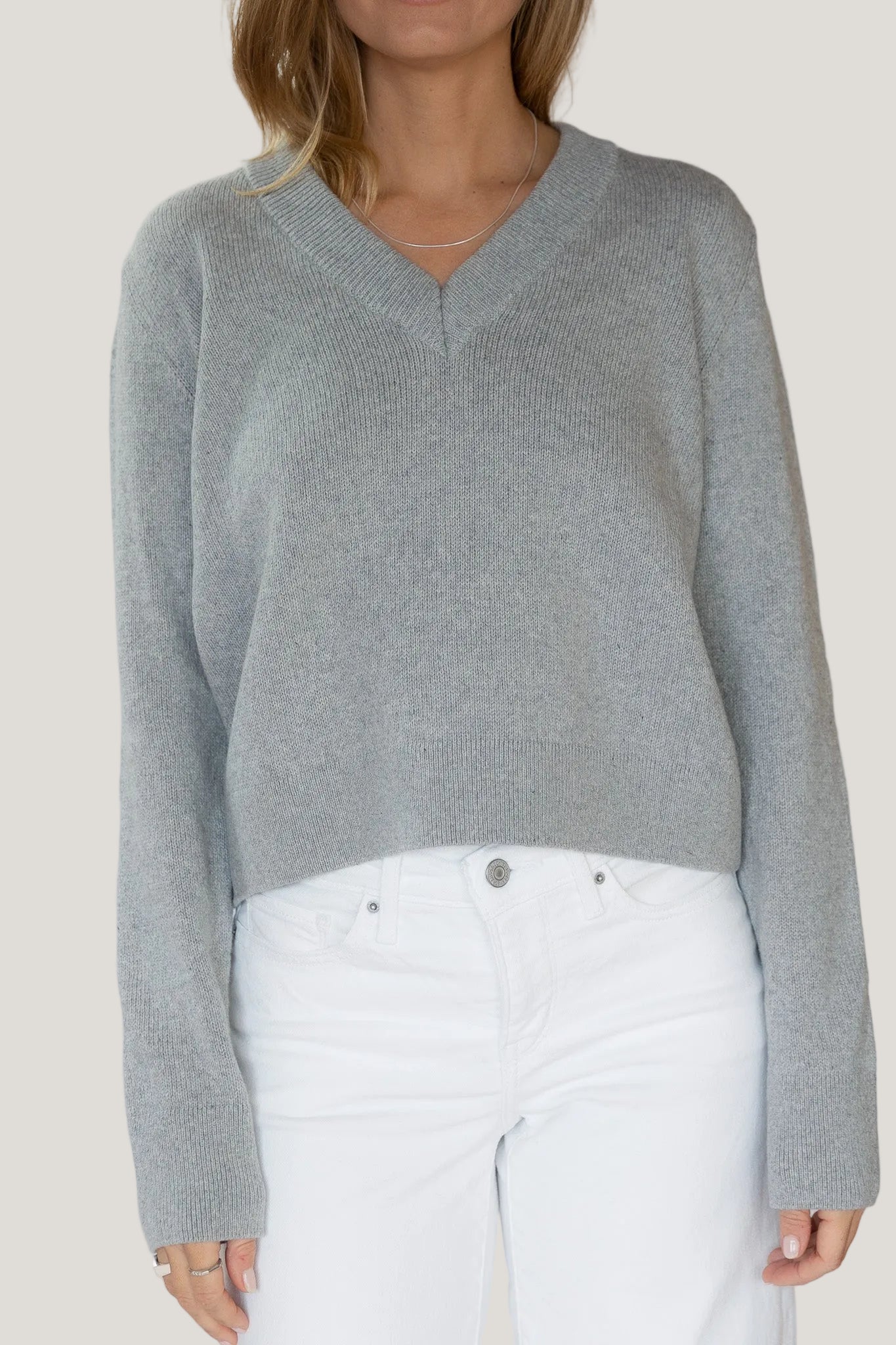 Person wearing a gray sweater and white pants on a plain background