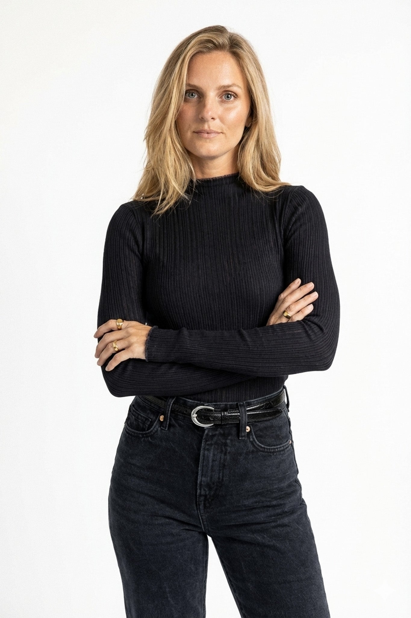 Woman wearing a black ribbed sweater and dark jeans on a white background