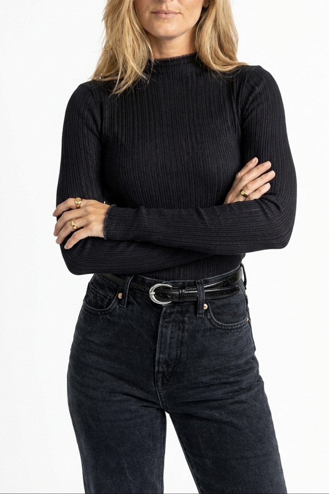 Woman wearing a black ribbed sweater and dark jeans on a white background