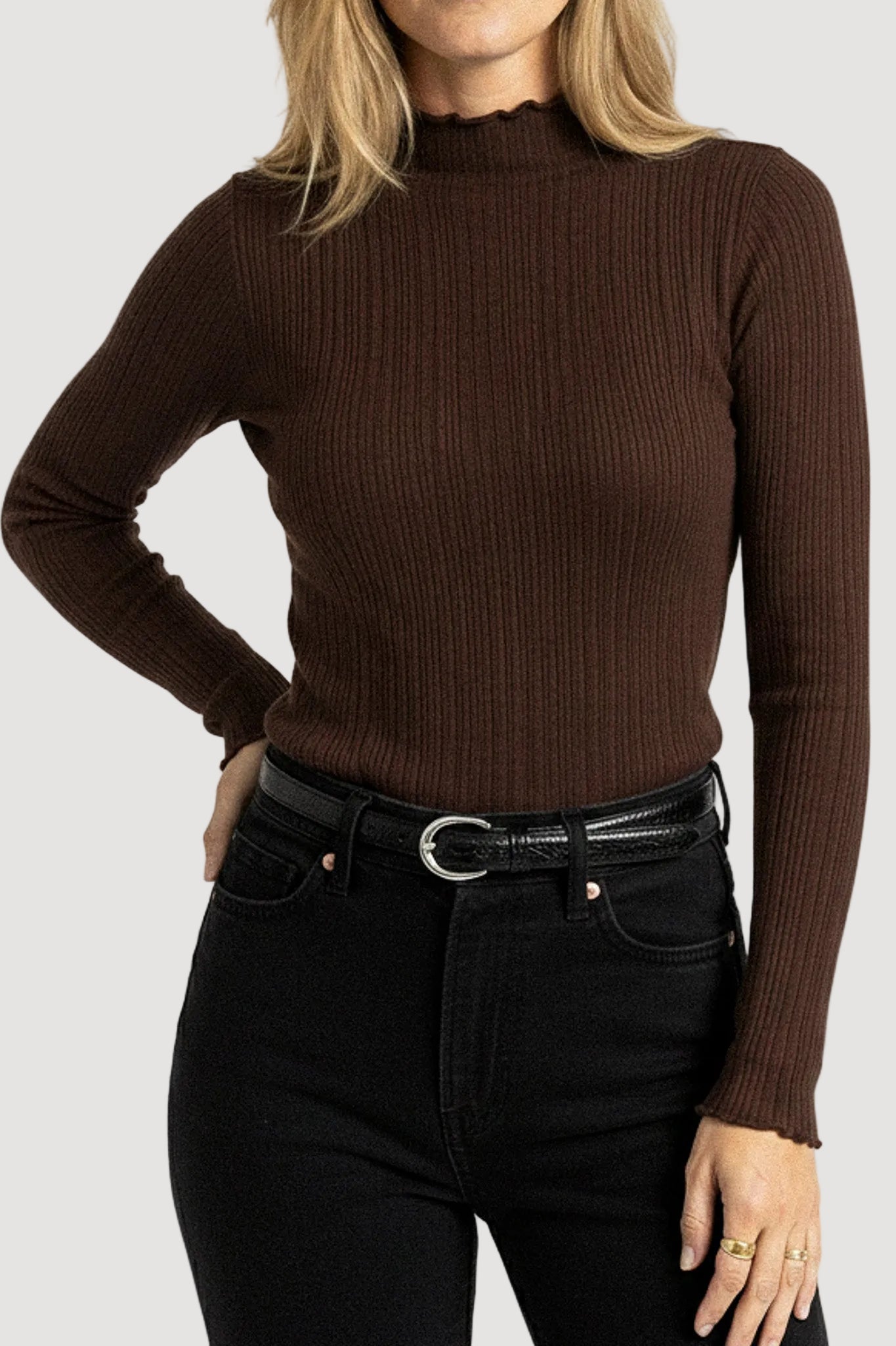 Person wearing a brown ribbed sweater and black jeans on a white background