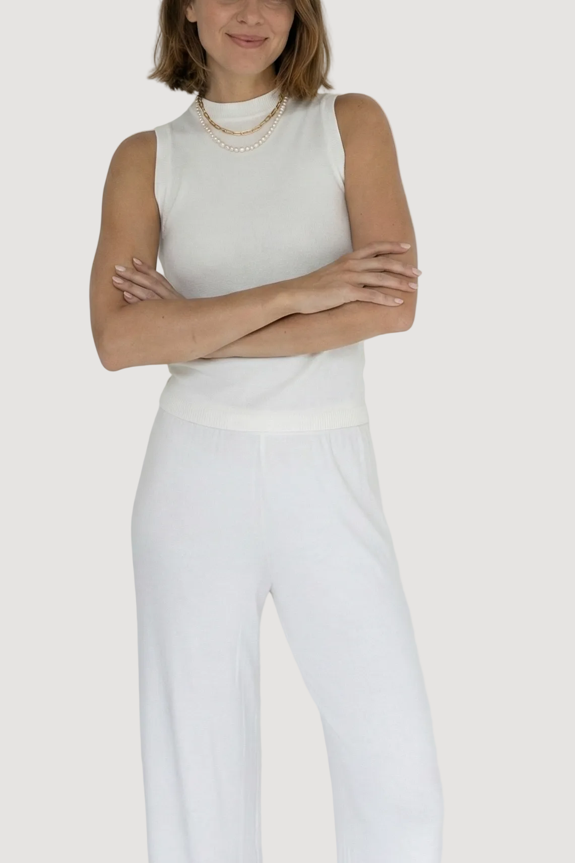 Woman wearing a white sleeveless top and pants against a plain background