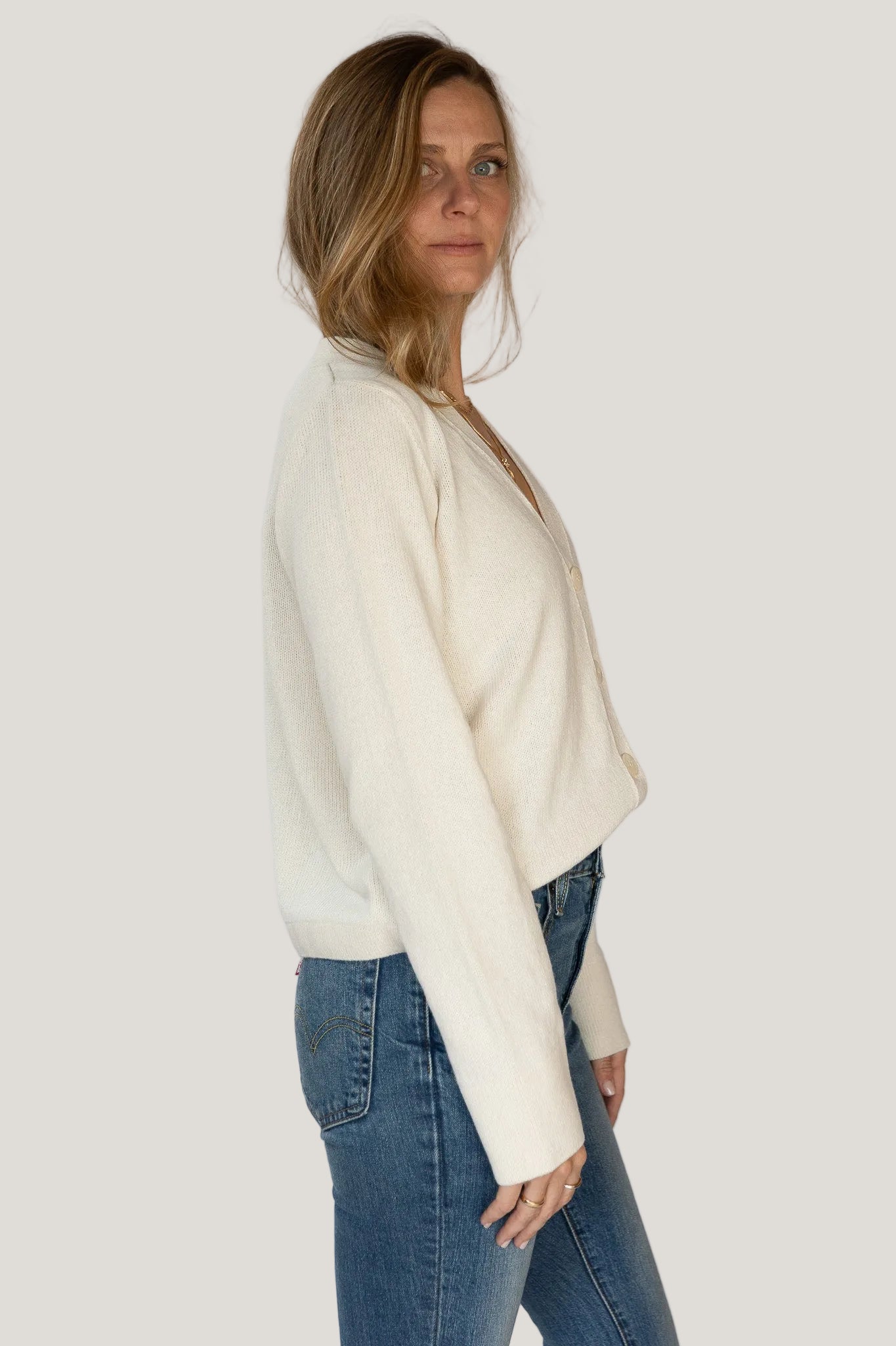 Woman wearing a cream sweater and blue jeans against a white background