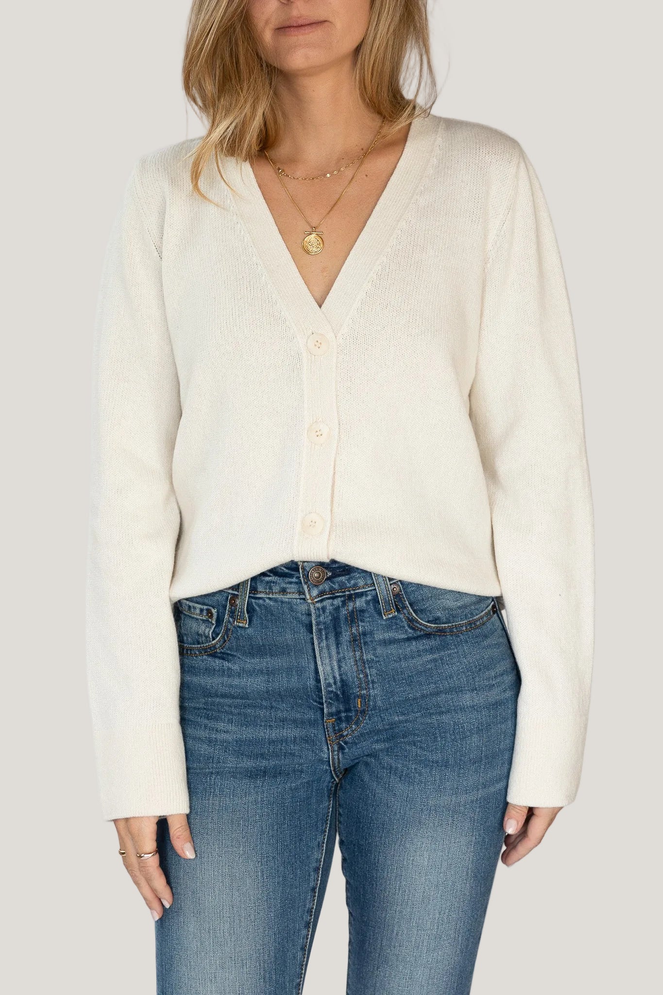Person wearing a cream cardigan and blue jeans on a white background