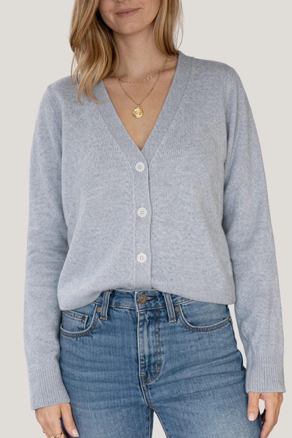 Person wearing a light gray cardigan and blue jeans against a white background