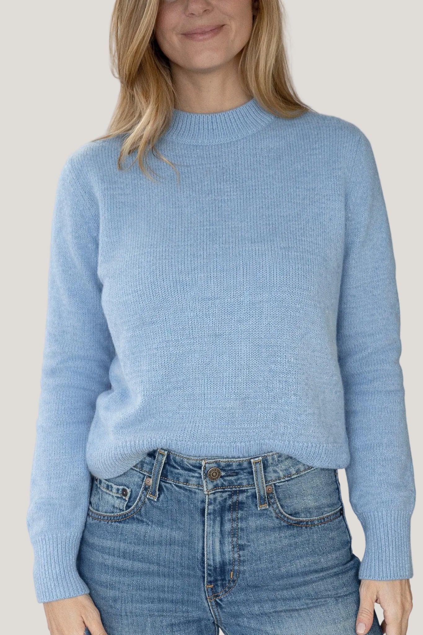 Person wearing a light blue sweater and jeans against a plain background