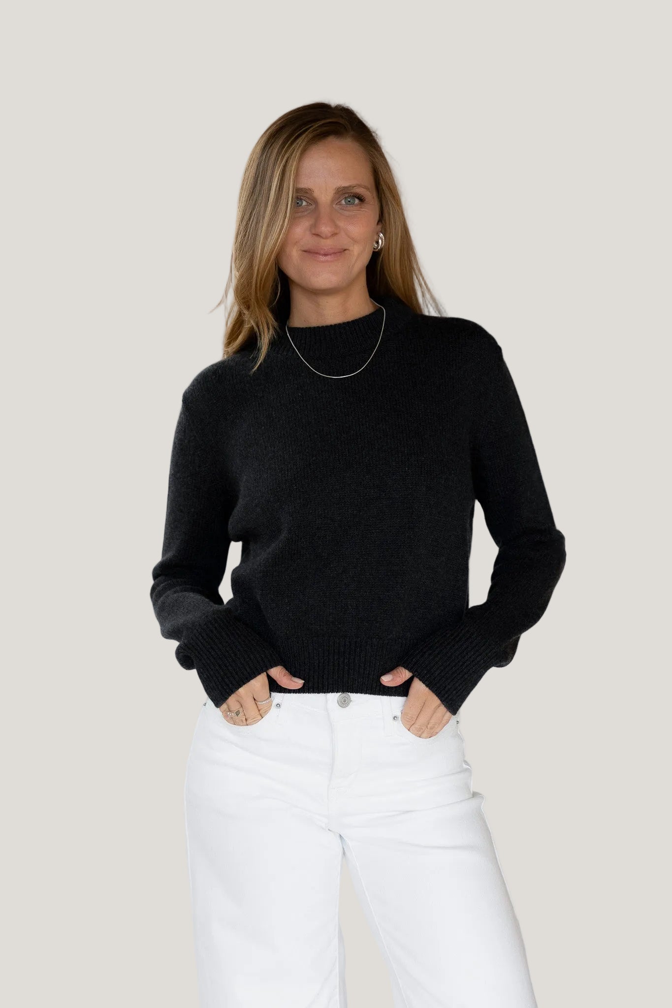 Woman wearing a black sweater and white pants against a white background
