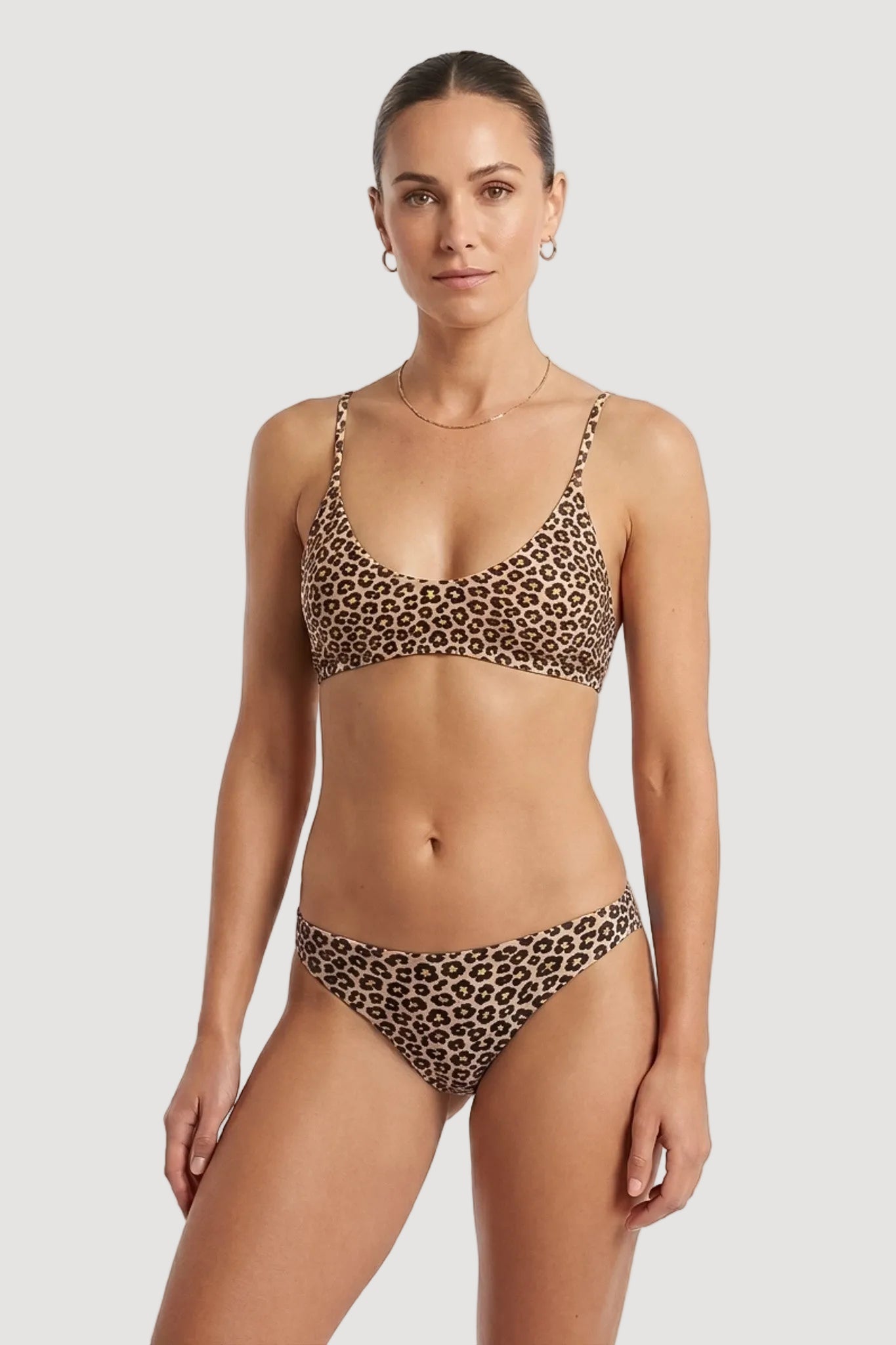 A woman modeling a two-piece bikini with a brown and black leopard print pattern against a plain white studio background.