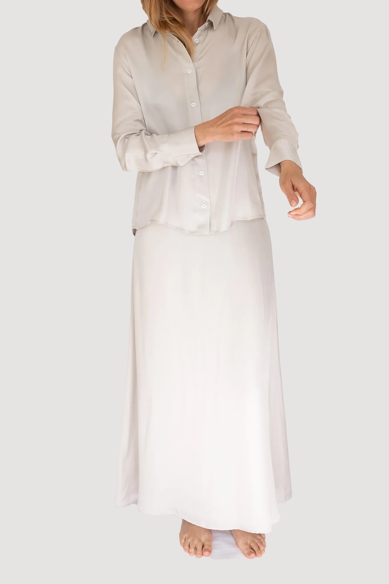 A model wearing a flowy maxi skirt with a high-rise fit and a narrow waistband, made from a blend of Tencel and Viscose, in a pearl white color.