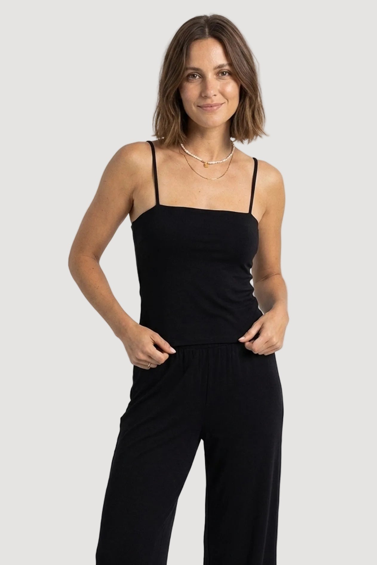 Woman wearing a black sleeveless top and black pants on a white background
