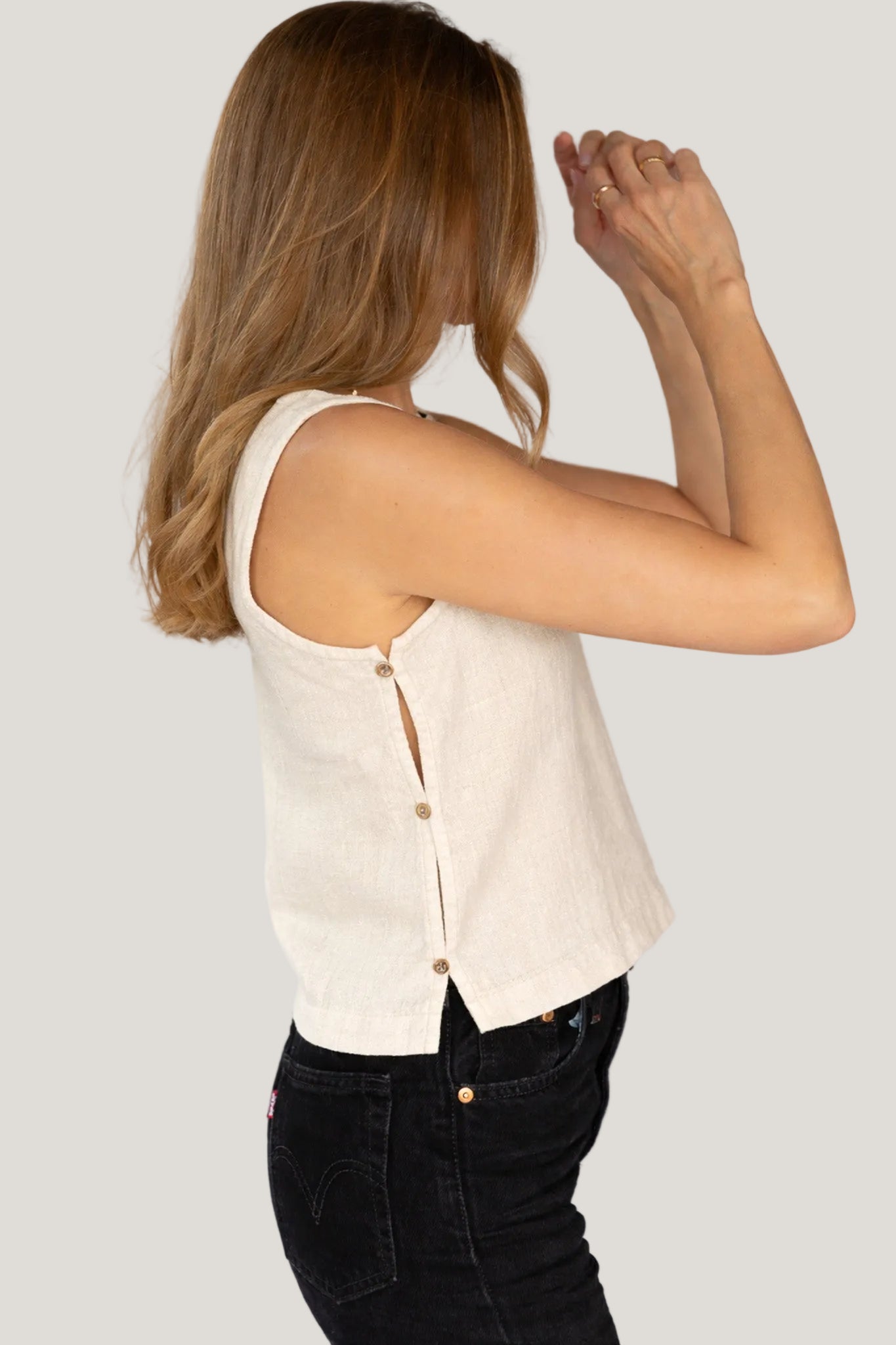Woman wearing a beige sleeveless top with button details on a plain background