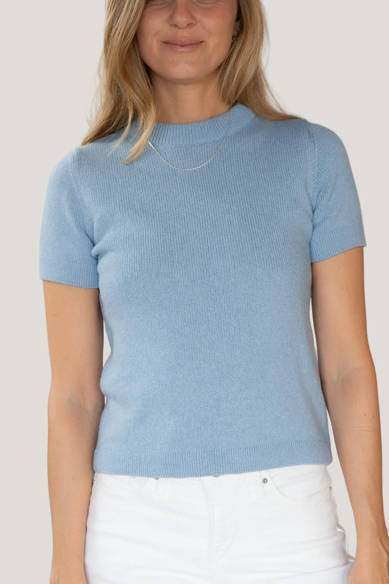 Woman wearing a light blue short-sleeve sweater against a white background
